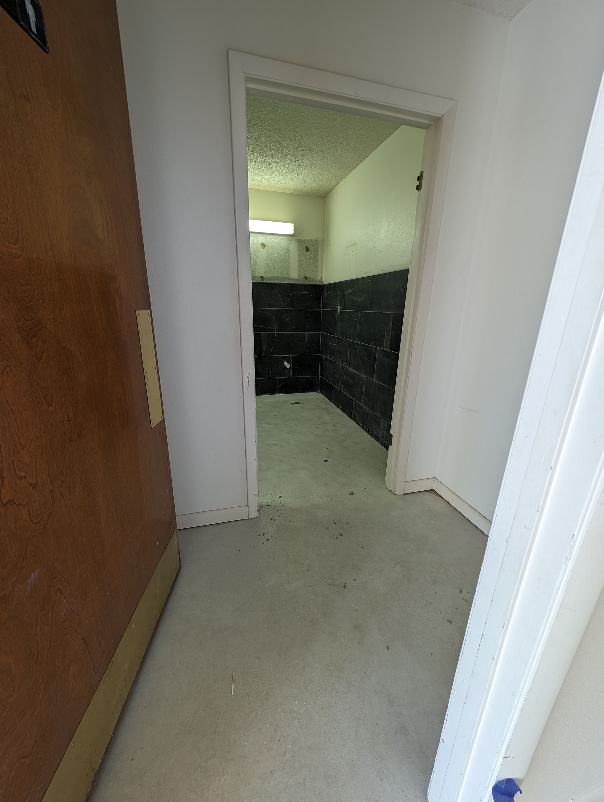 Narrow hallway with white walls and a doorway opening to a dark room with black cabinets.
