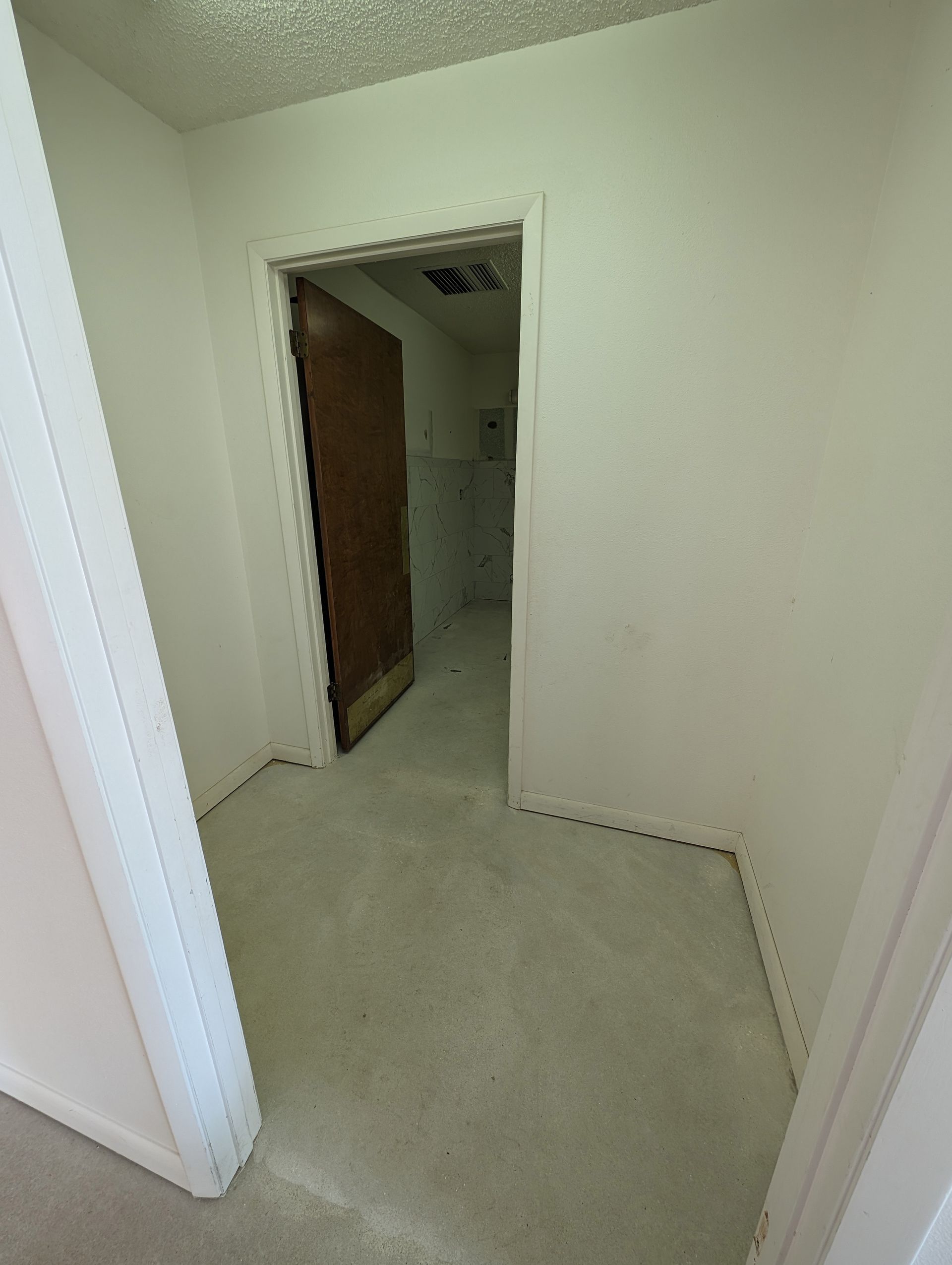 Empty white hallway with a doorway opening into a darker room and a brown door inside
