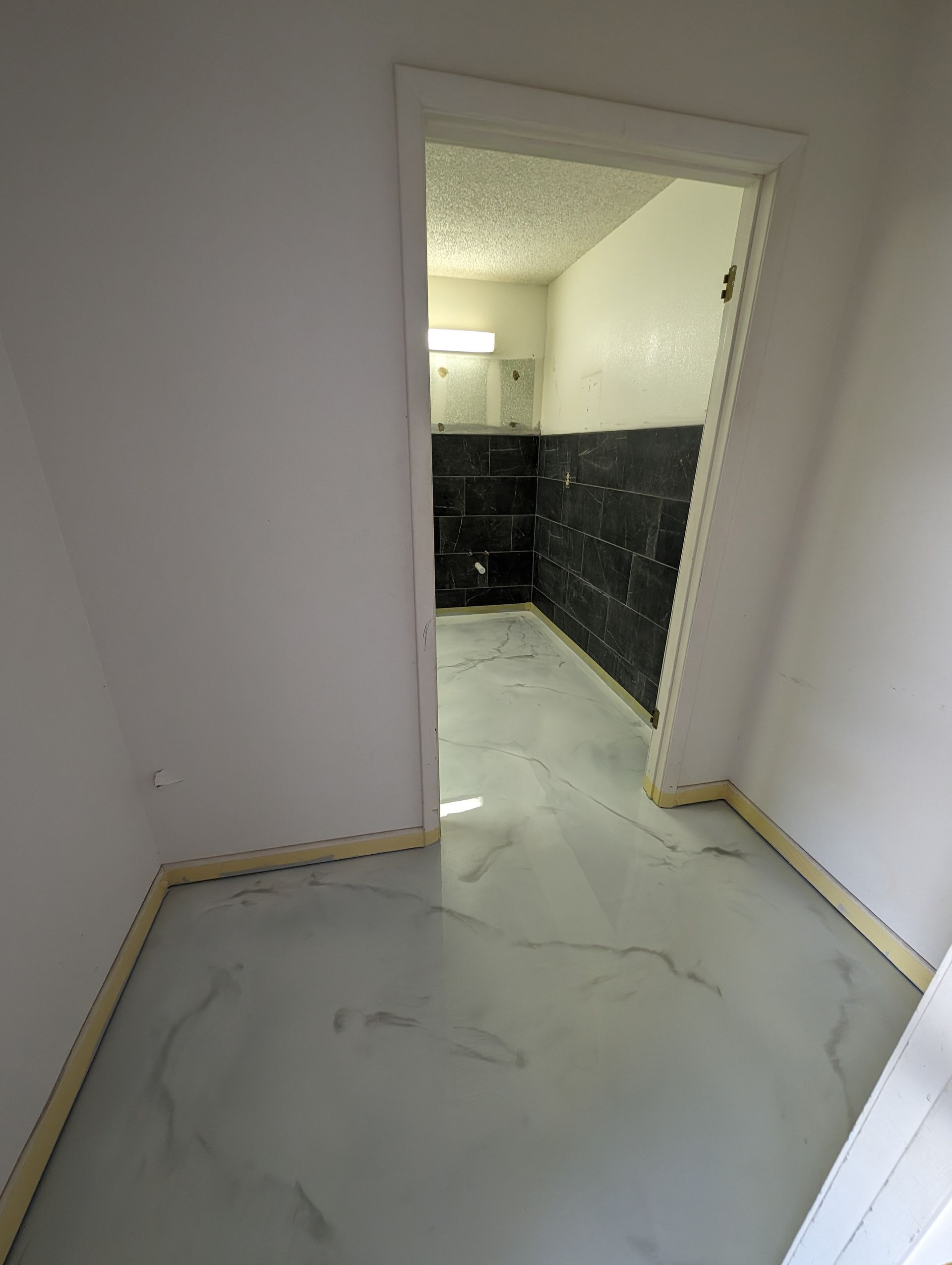 Empty hallway with white walls and marble-look floor leading to a doorway into a tiled room