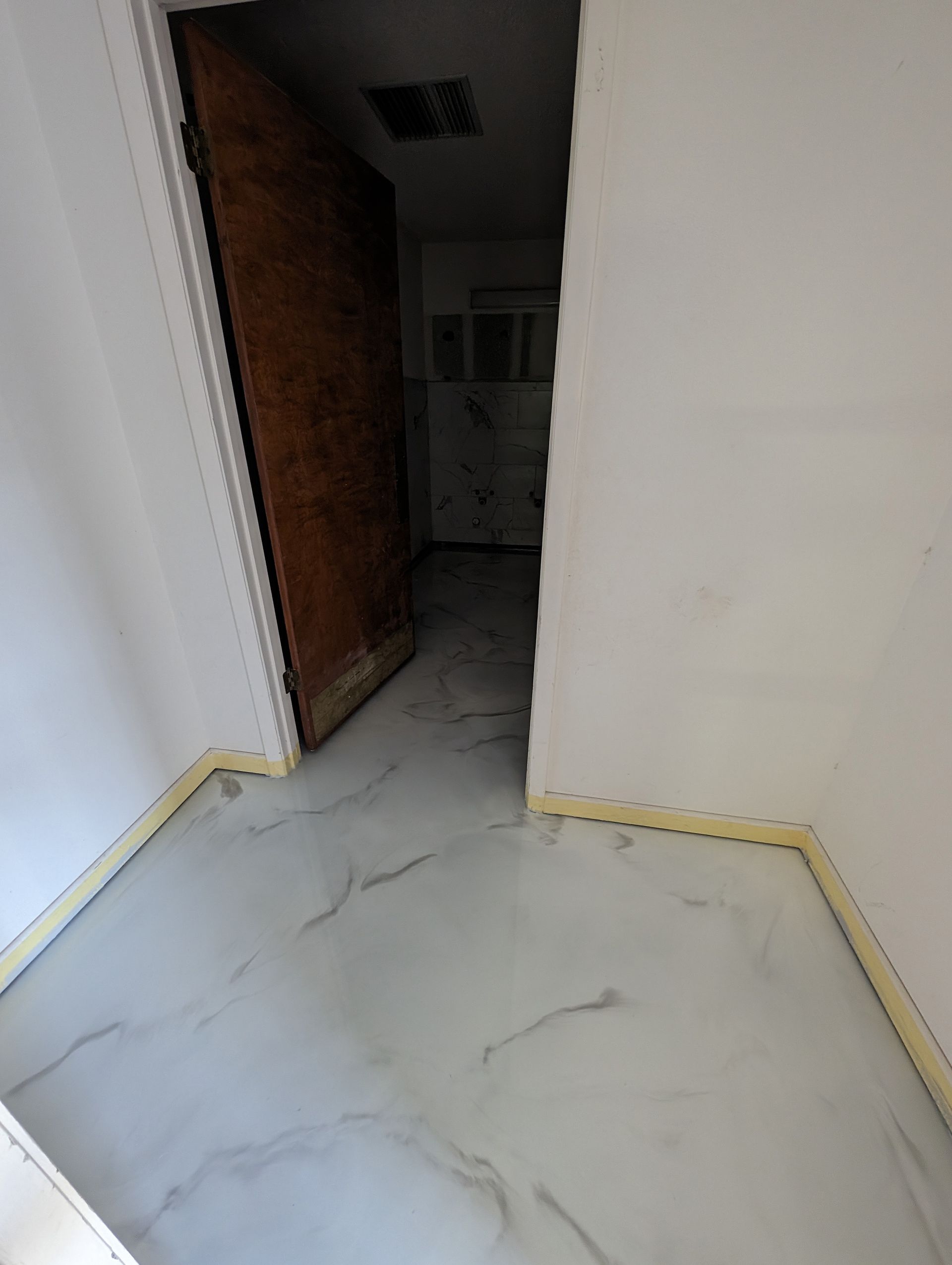 Empty unfinished room with white marble floor, yellow tape edges, and a dark doorway leading to a dim hall