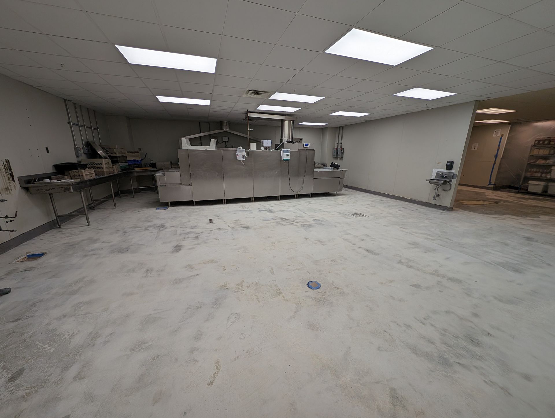 Empty fluorescent-lit room with tiled floor, counters, and scattered equipment near the walls.