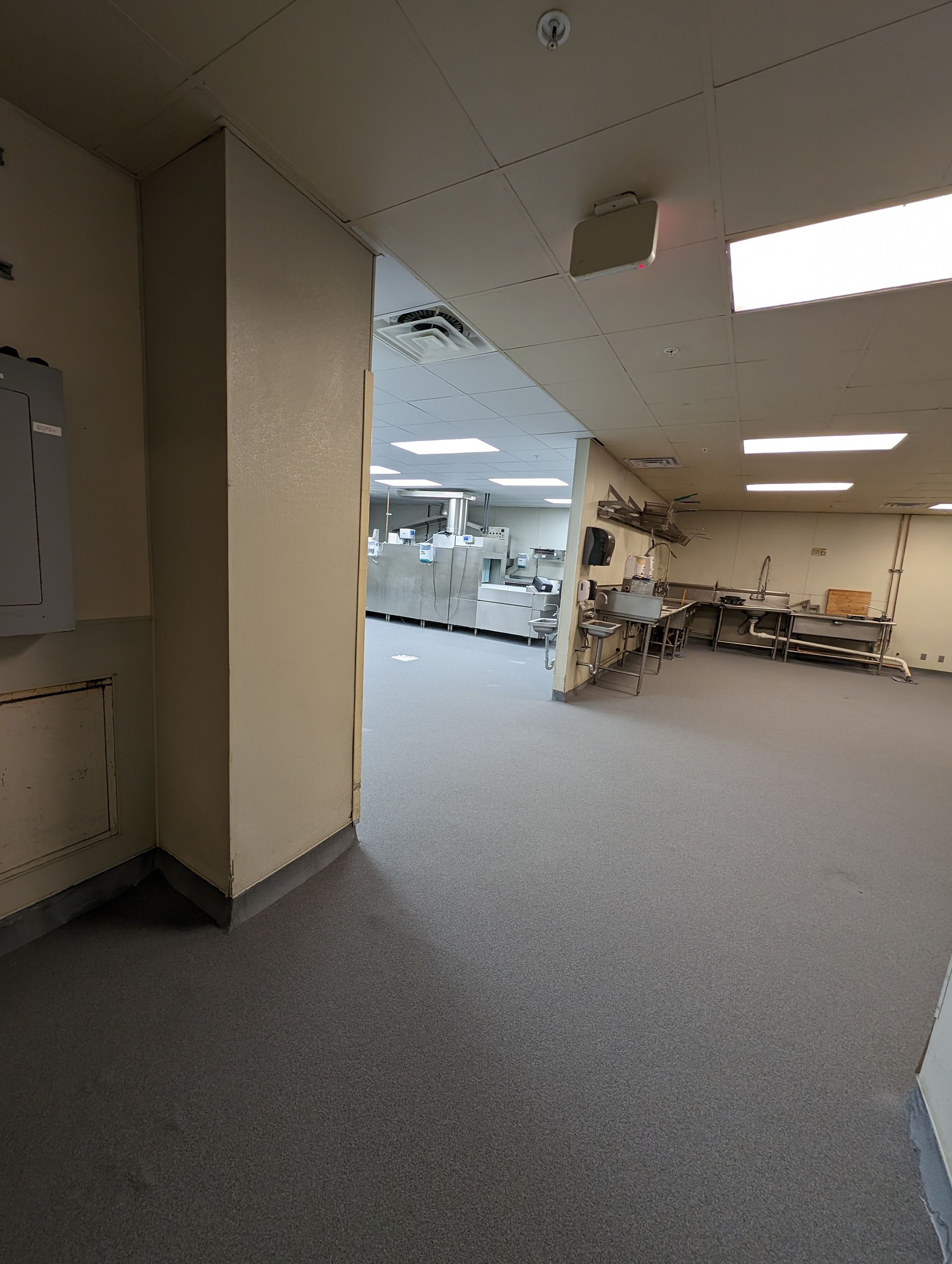 Damaged office hallway with debris on the floor and exposed ceiling, leading into a bright workspace