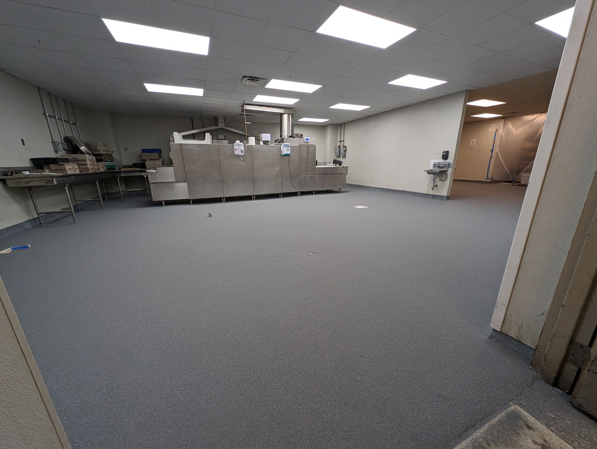 Empty office space with gray carpet, fluorescent ceiling lights, cubicles, and a hallway on the right.