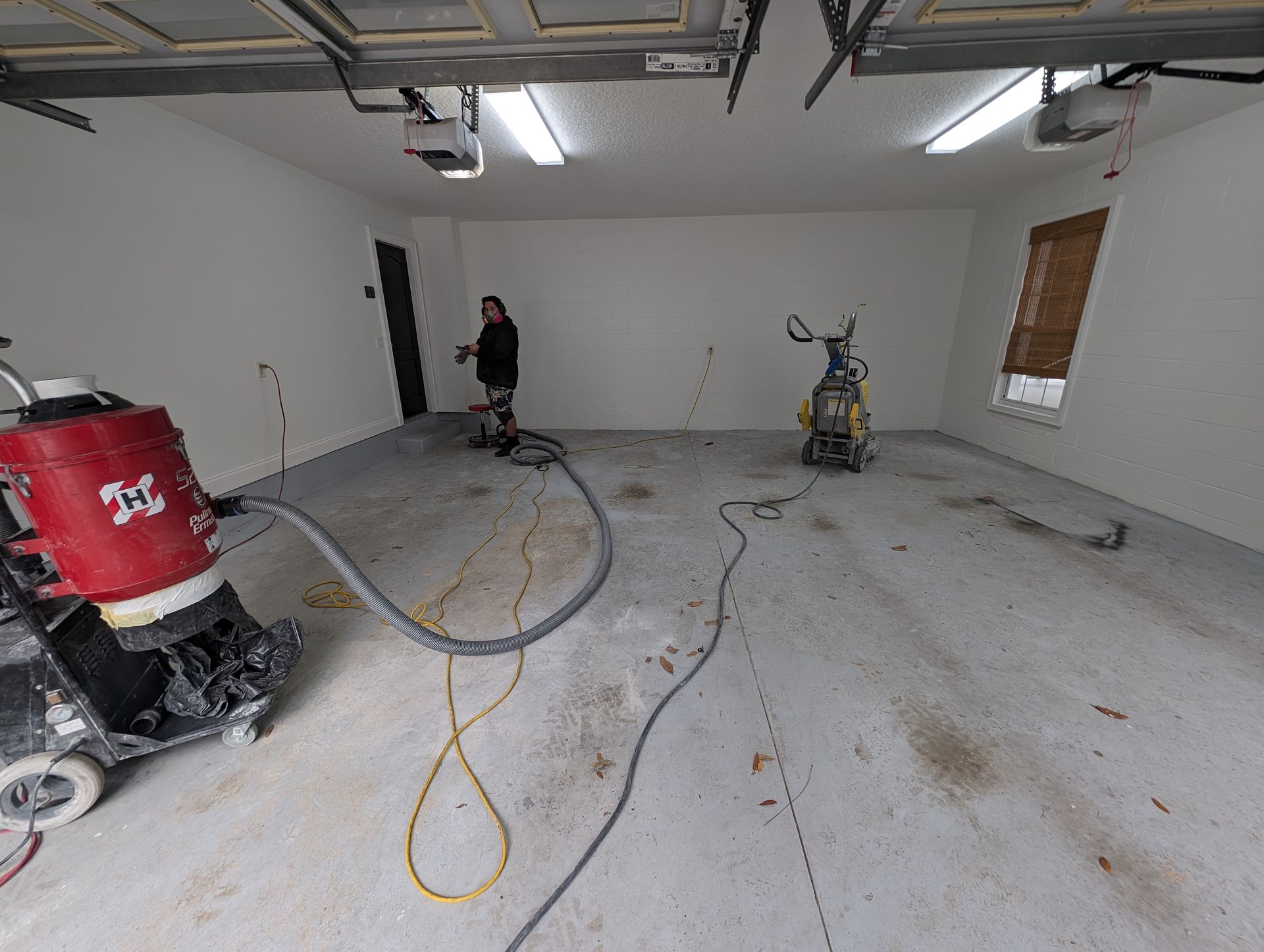 Partially renovated garage with dusty concrete floor, tools, and a person standing near the back wall