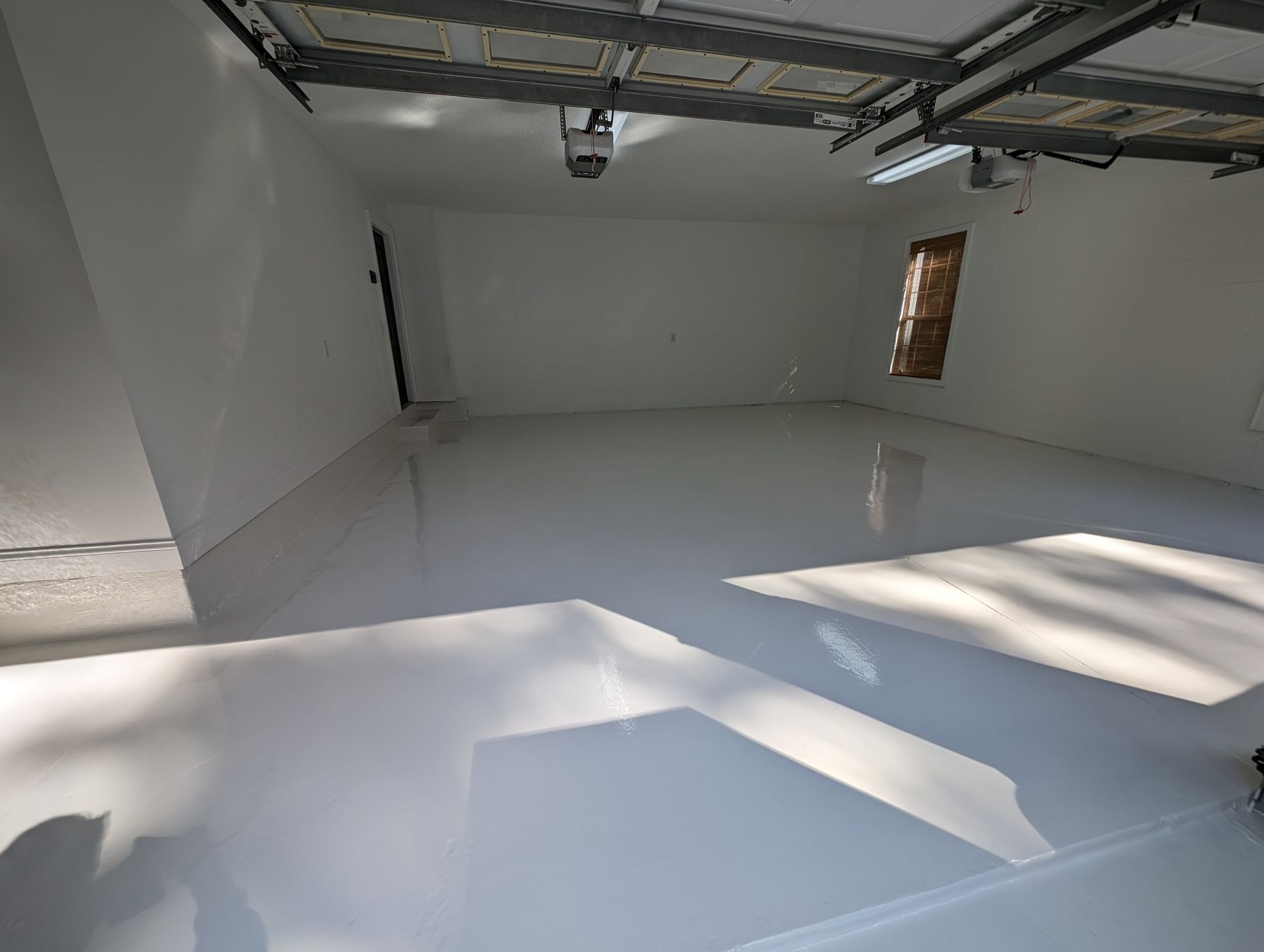 Empty white garage with glossy floor and sunlight streaming through the open door.