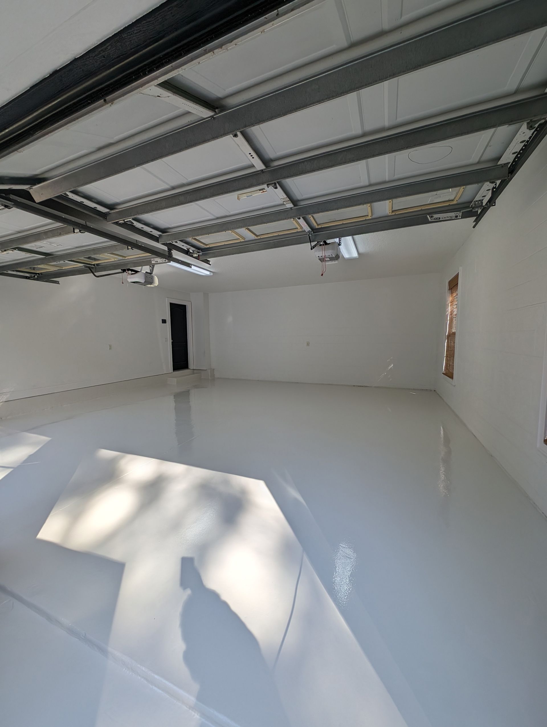 Empty white garage interior with open metal ceiling and sunlight casting shadows on the floor
