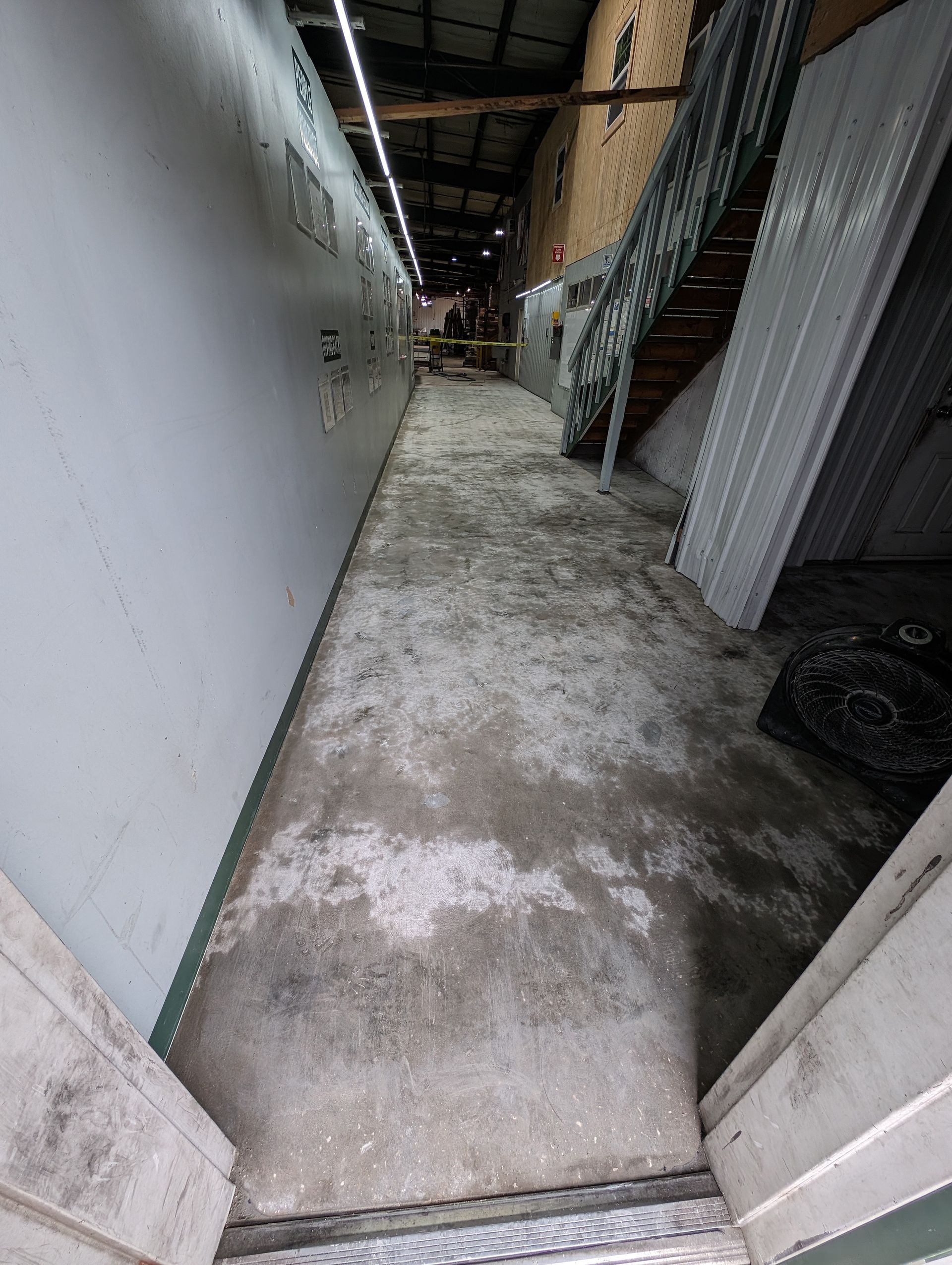 Narrow concrete alleyway with white walls and a metal staircase, leading to a dim interior space.