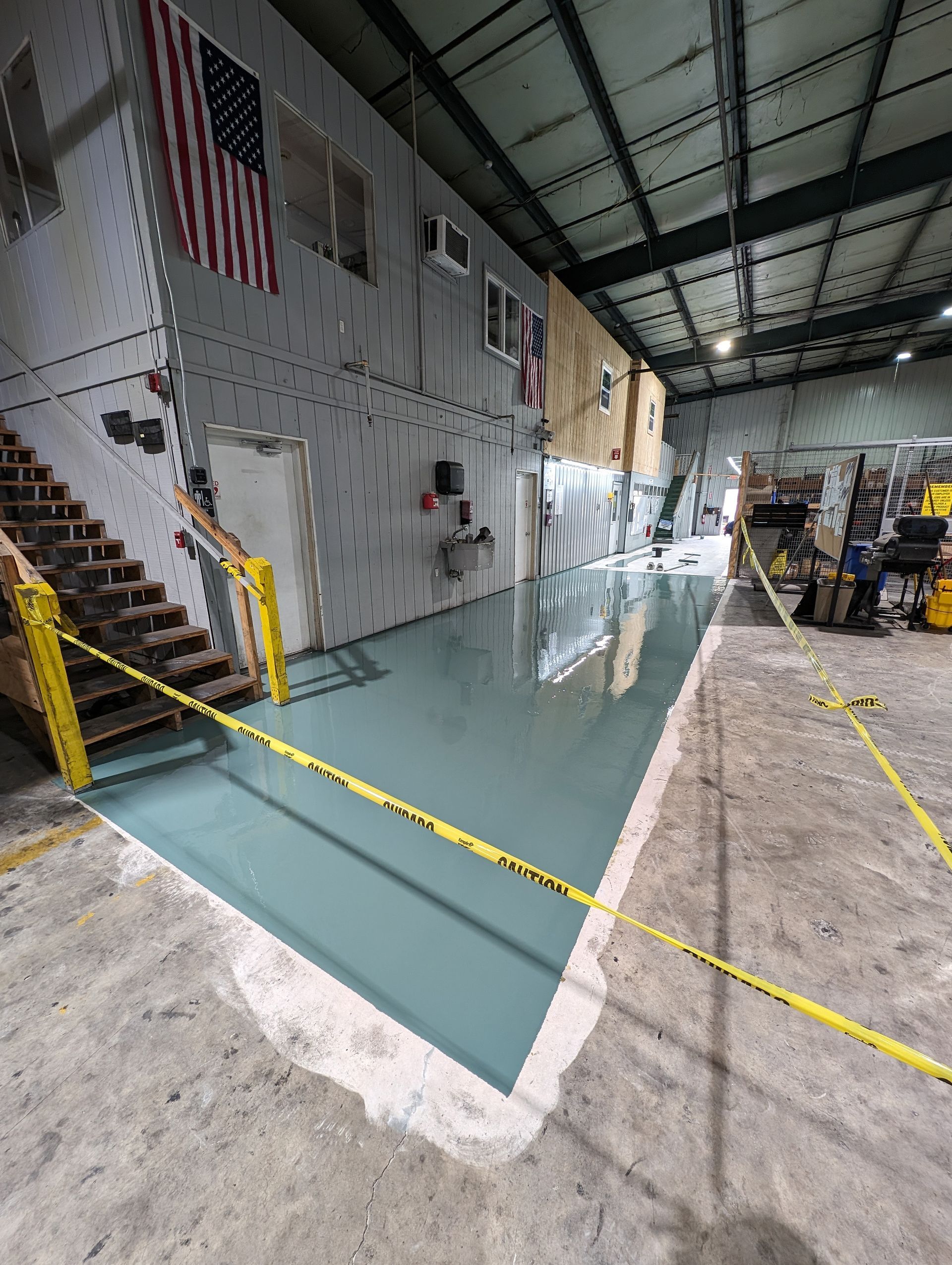 Large indoor warehouse with a flooded concrete floor and yellow caution tape blocking the area