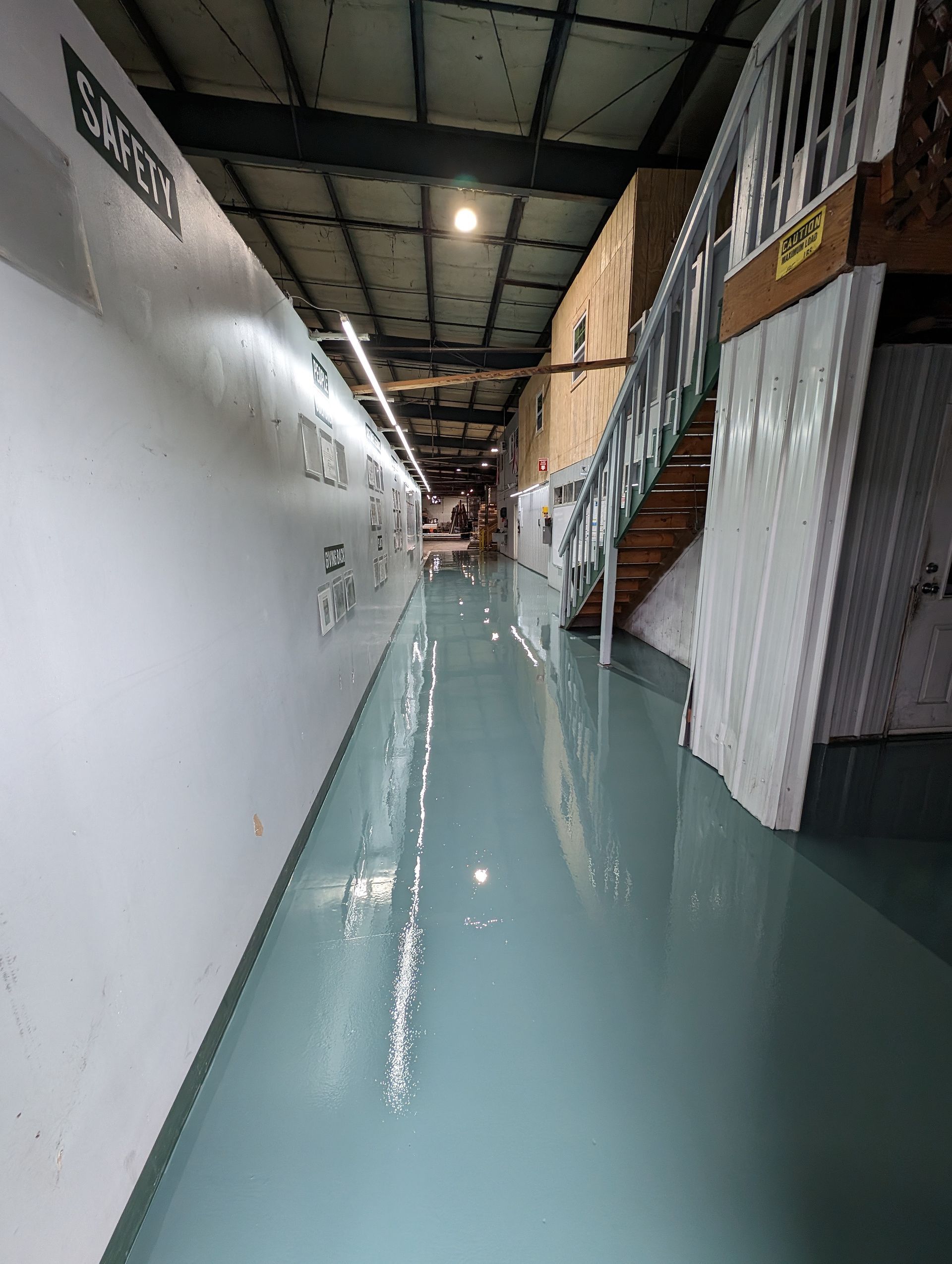 Empty industrial hallway with glossy green floor, white walls, and stairs along the right side