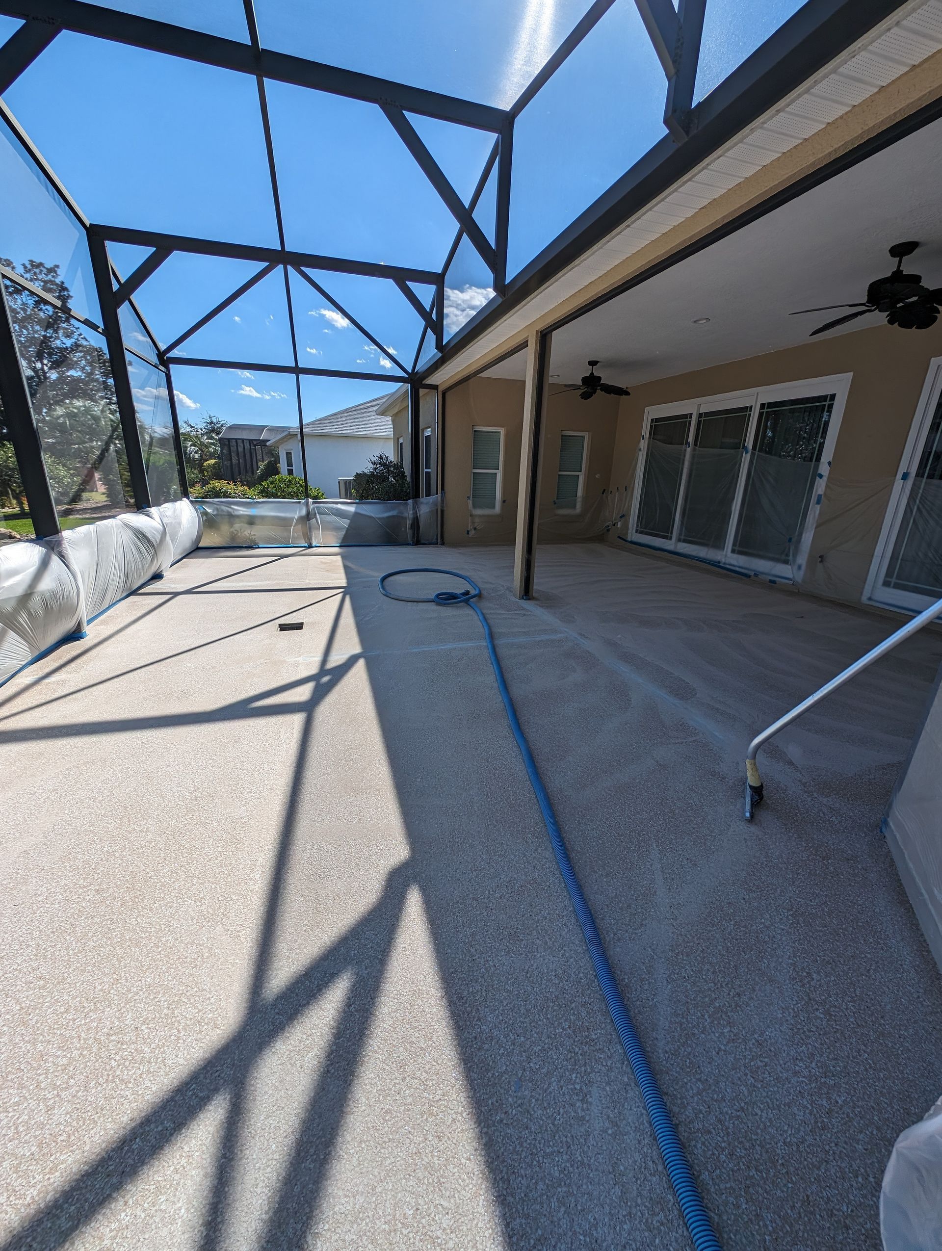 Covered patio with screened enclosure, sliding doors, and a blue hose on a sunlit concrete floor