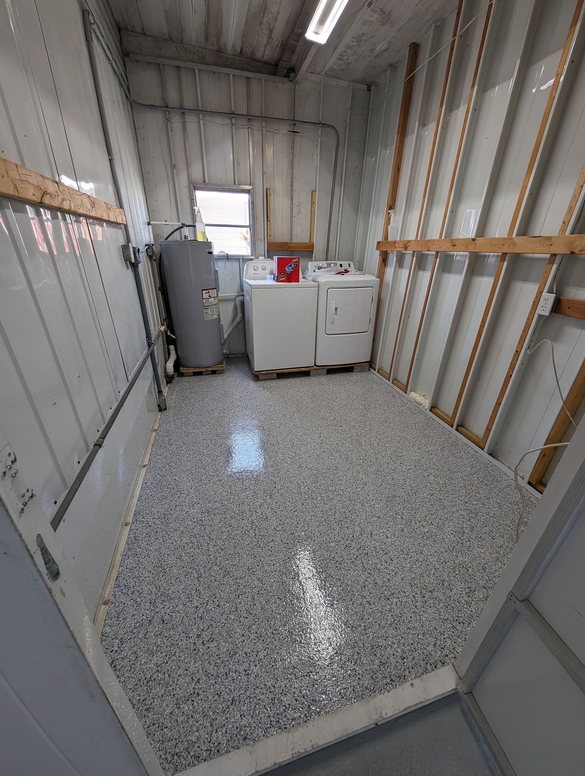 Small storage room with washer, dryer, utility cabinet, and speckled floor under bright overhead lights.