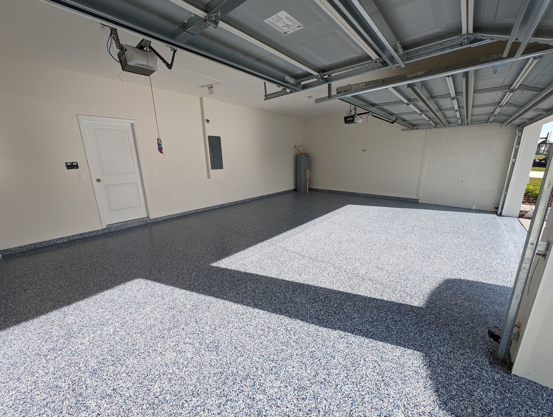 Empty garage with speckled gray floor, white walls, and an open door letting in sunlight