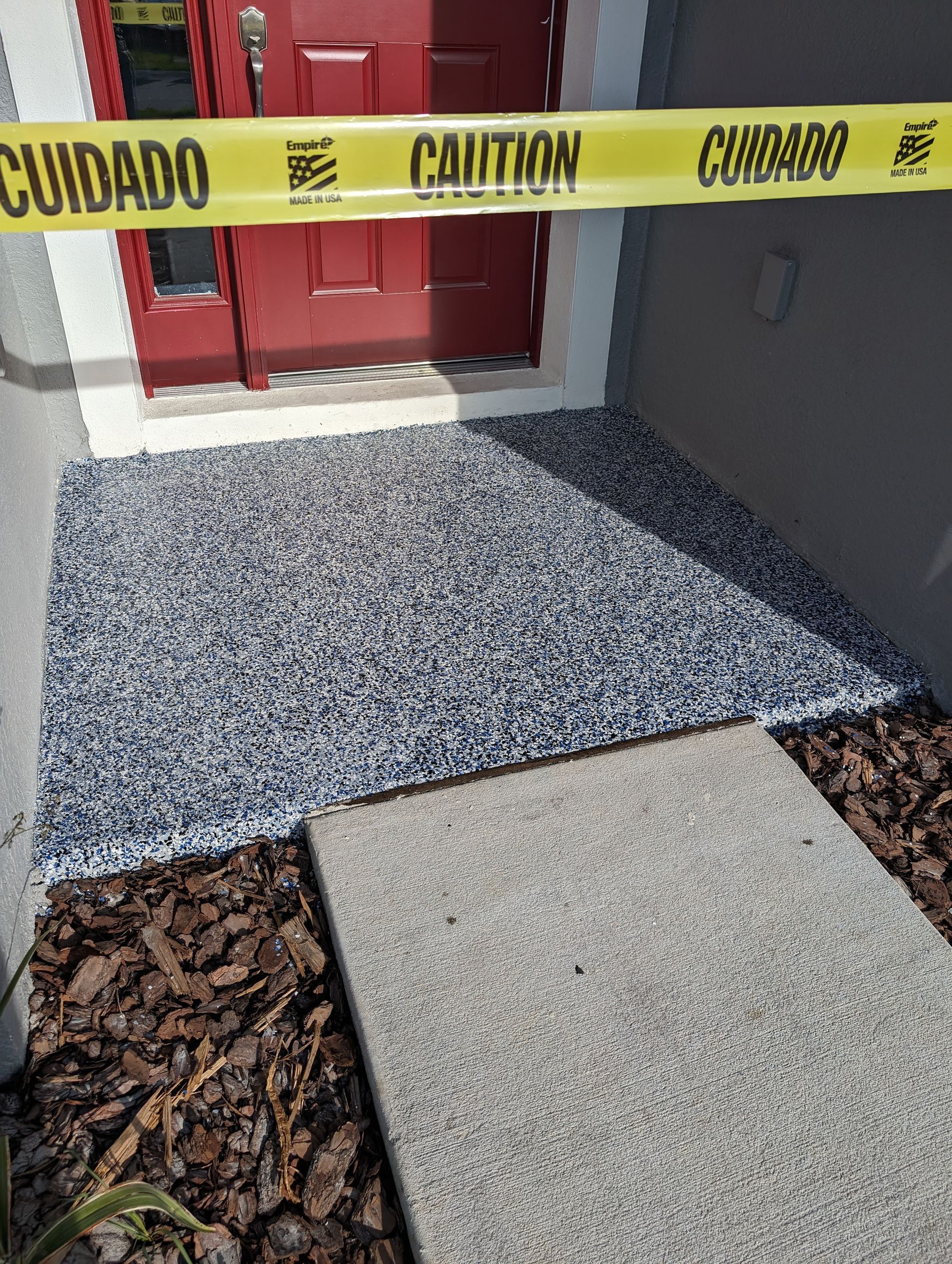 Caution tape blocks a red door with a newly poured concrete ramp and walkway outside.