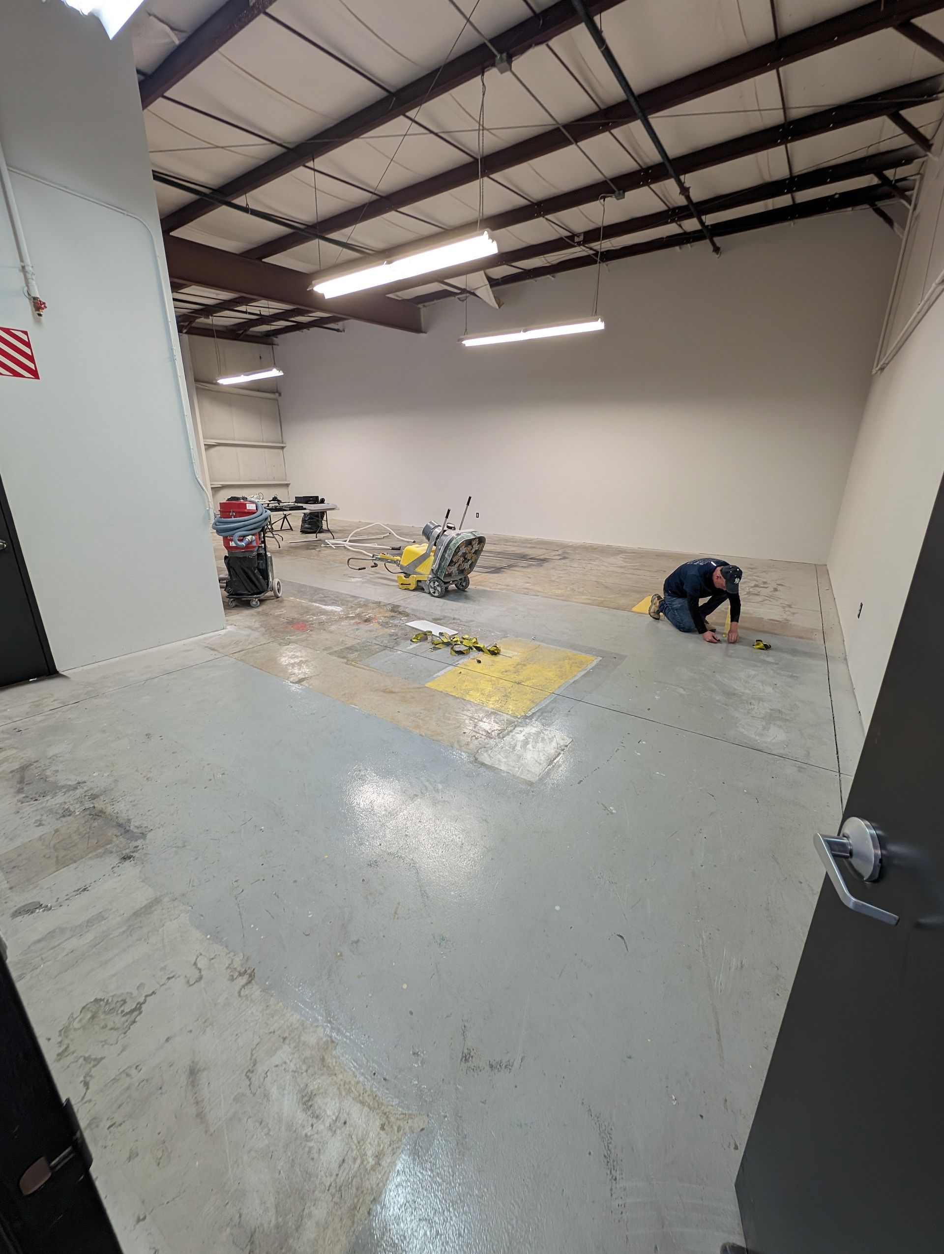 Empty industrial warehouse with concrete floor, exposed beams, and workers near the back wall
