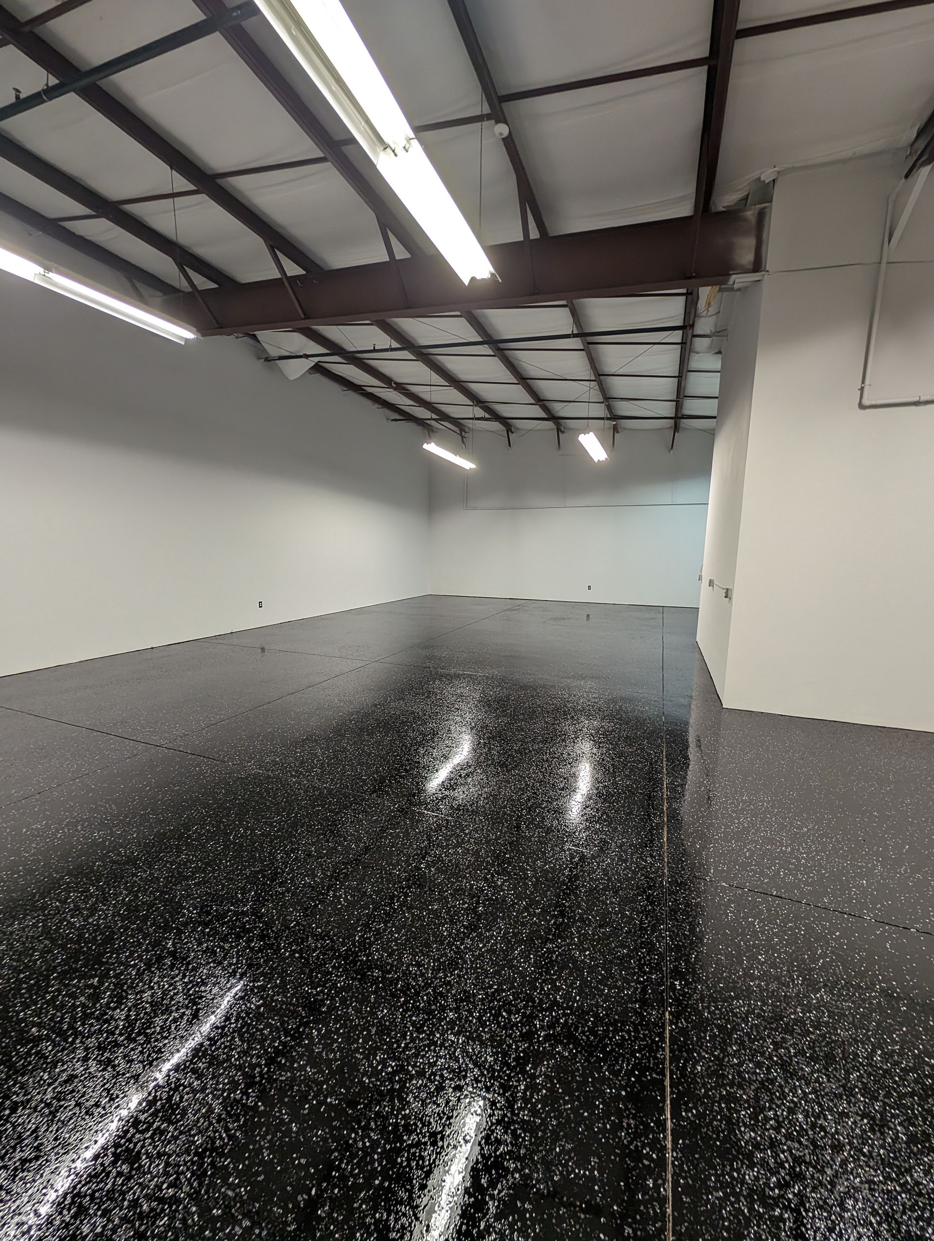 Empty industrial warehouse with glossy black speckled floor and bright overhead lights
