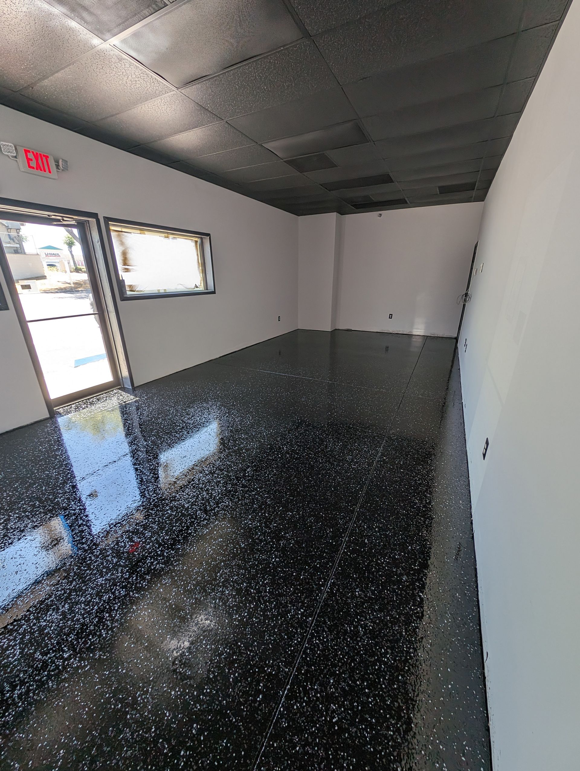 Empty room with glossy black floor, white walls, and an open door with daylight