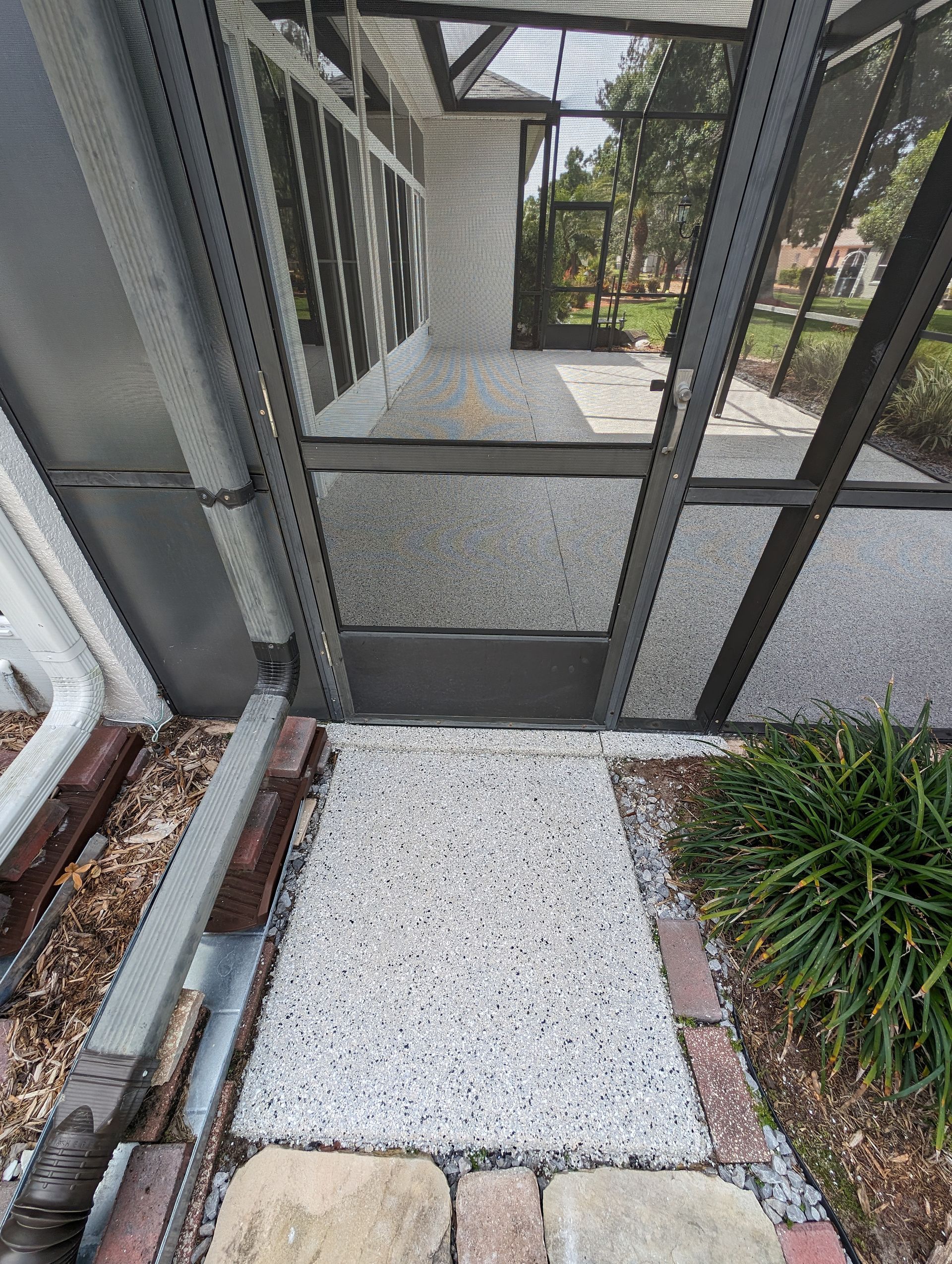 Gravel path leading to a screened porch and metal gate beside a house entrance.