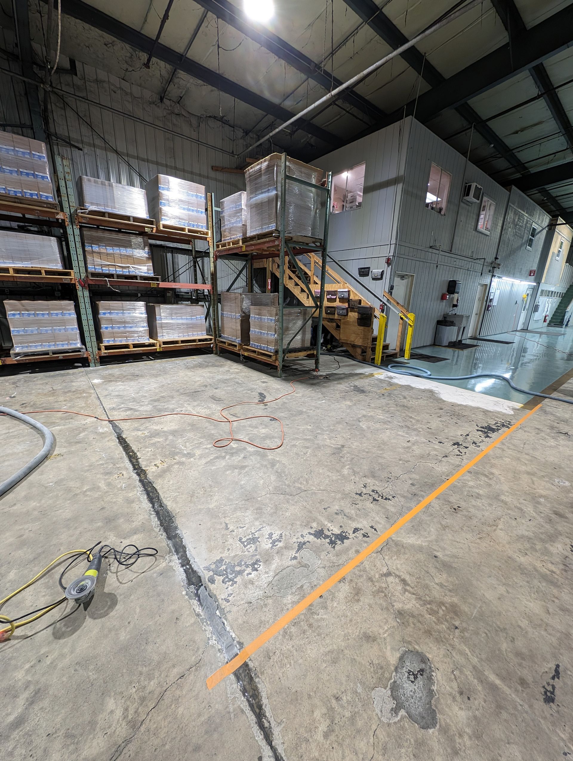 Industrial warehouse interior with stacked pallets, metal stairs, concrete floor, and marked safety lines