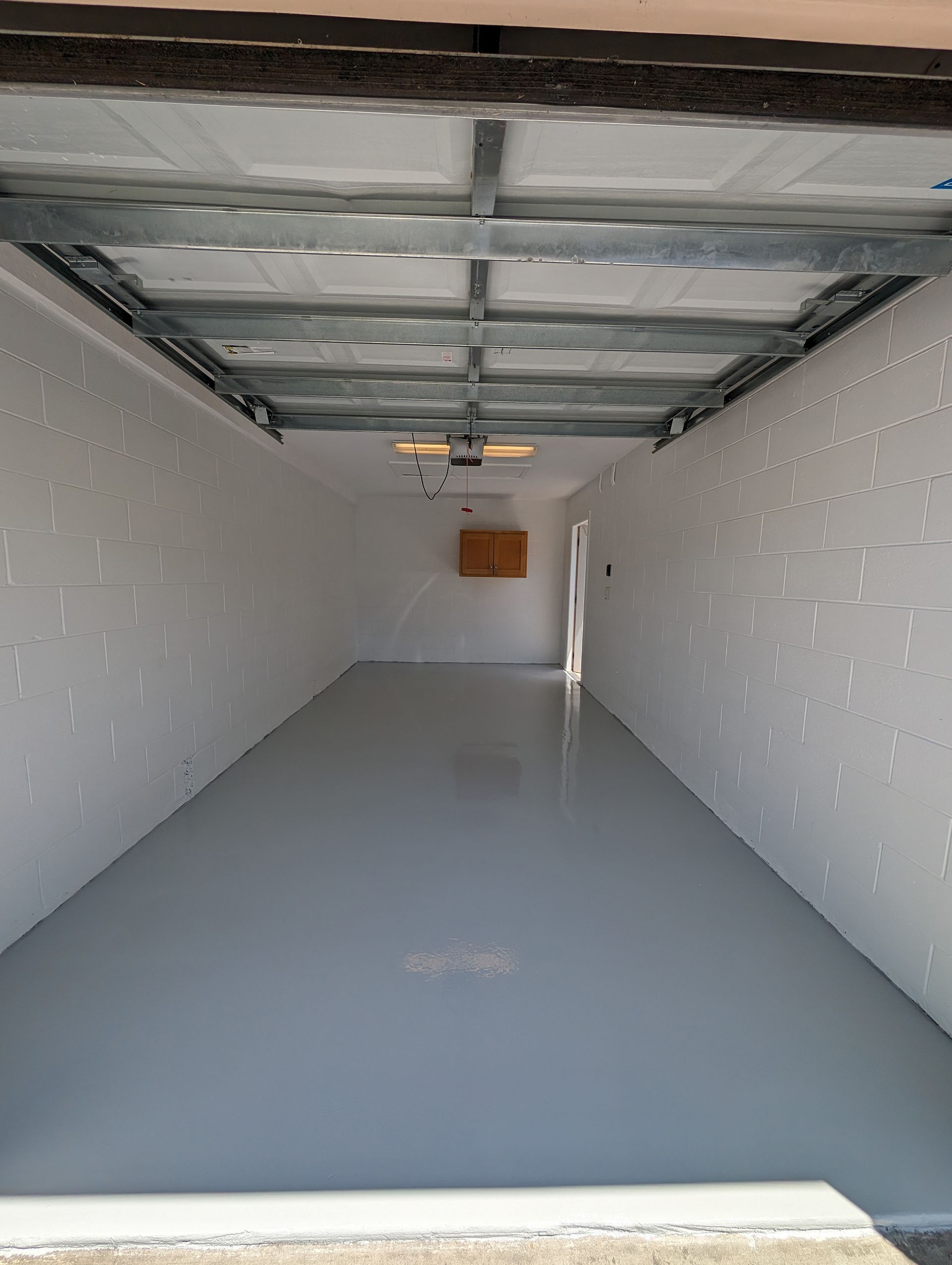 Empty garage interior with gray floor, white walls, and an open garage door.