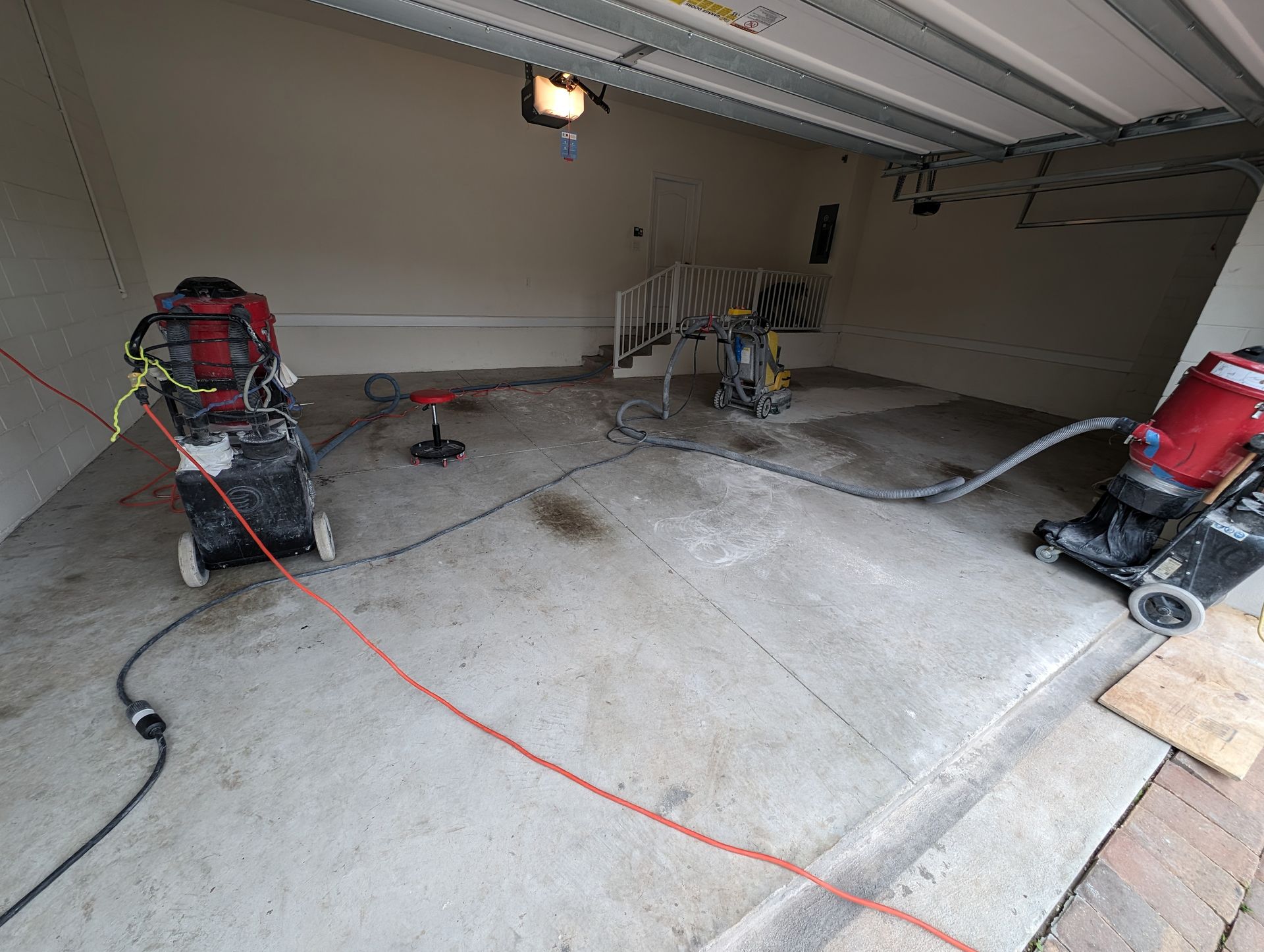 Garage with concrete floor, several power tools, extension cords, and a partially open garage door.