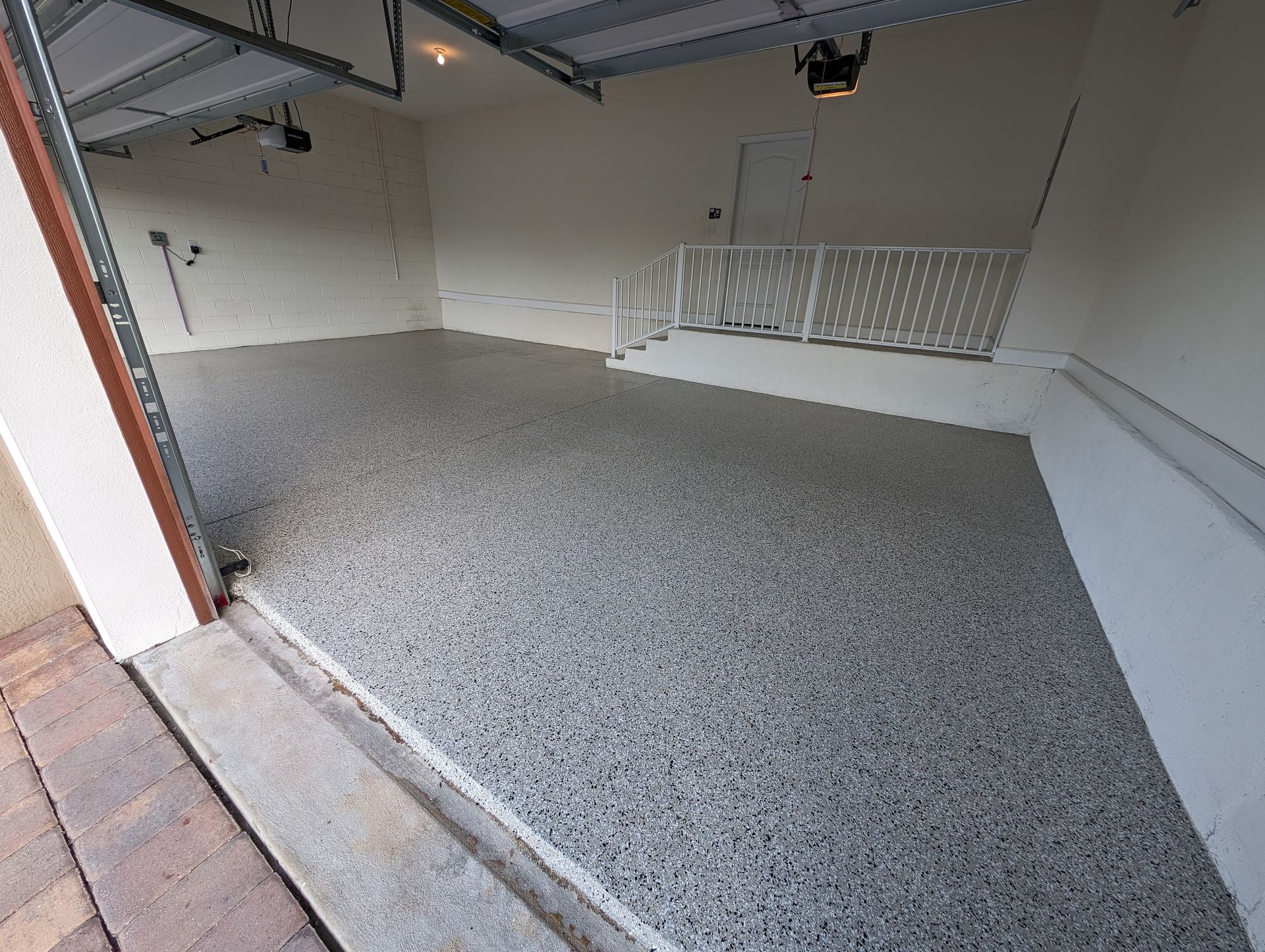 Empty garage with gray speckled floor and white walls, viewed from the open doorway
