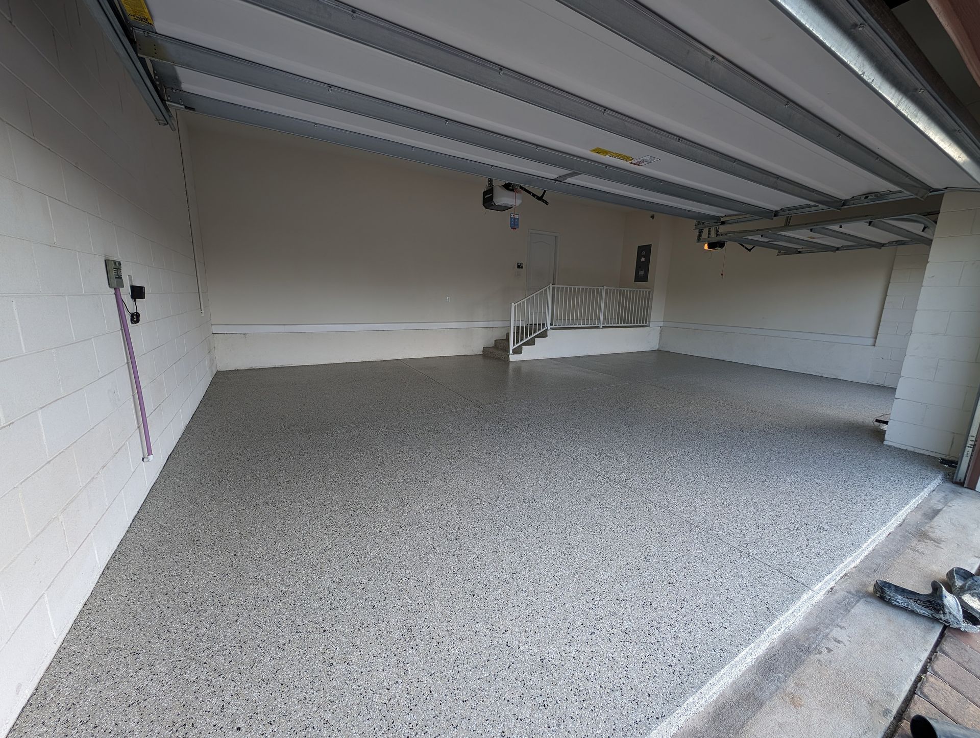 Empty garage interior with speckled floor, white walls, and an open ceiling door overhead