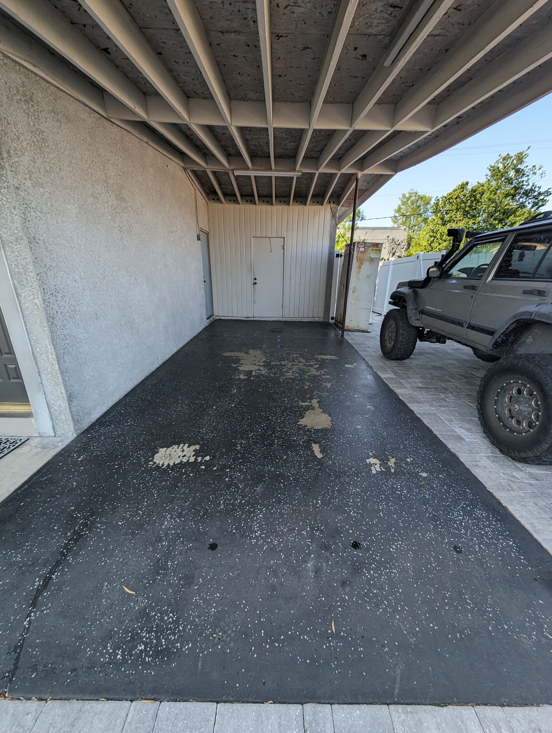 Covered parking area with a parked off-road vehicle beside a stucco wall and dark floor.