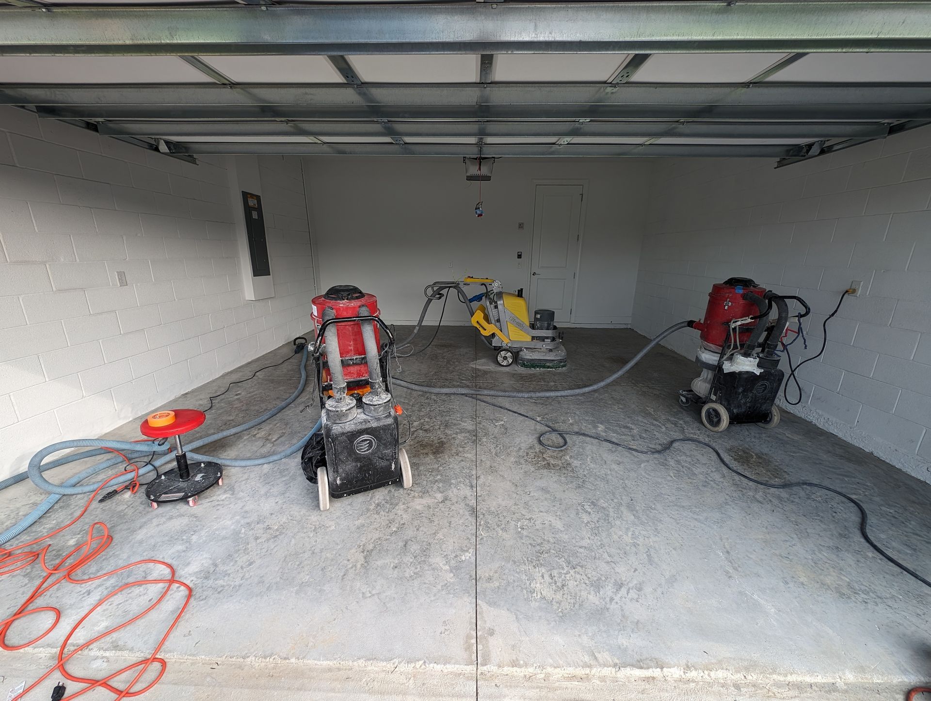 Garage with three concrete saws and coiled extension cords on the floor under a closed garage door