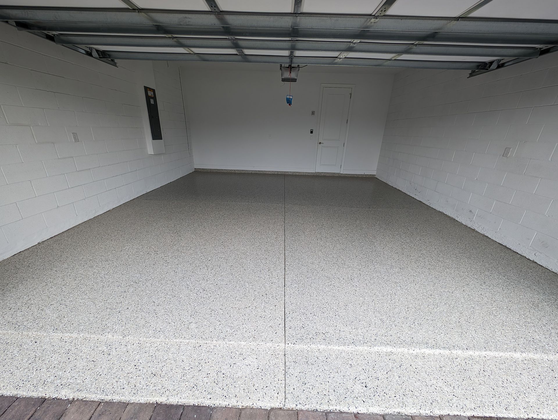 Empty garage with white walls, speckled floor, and an open ceiling.