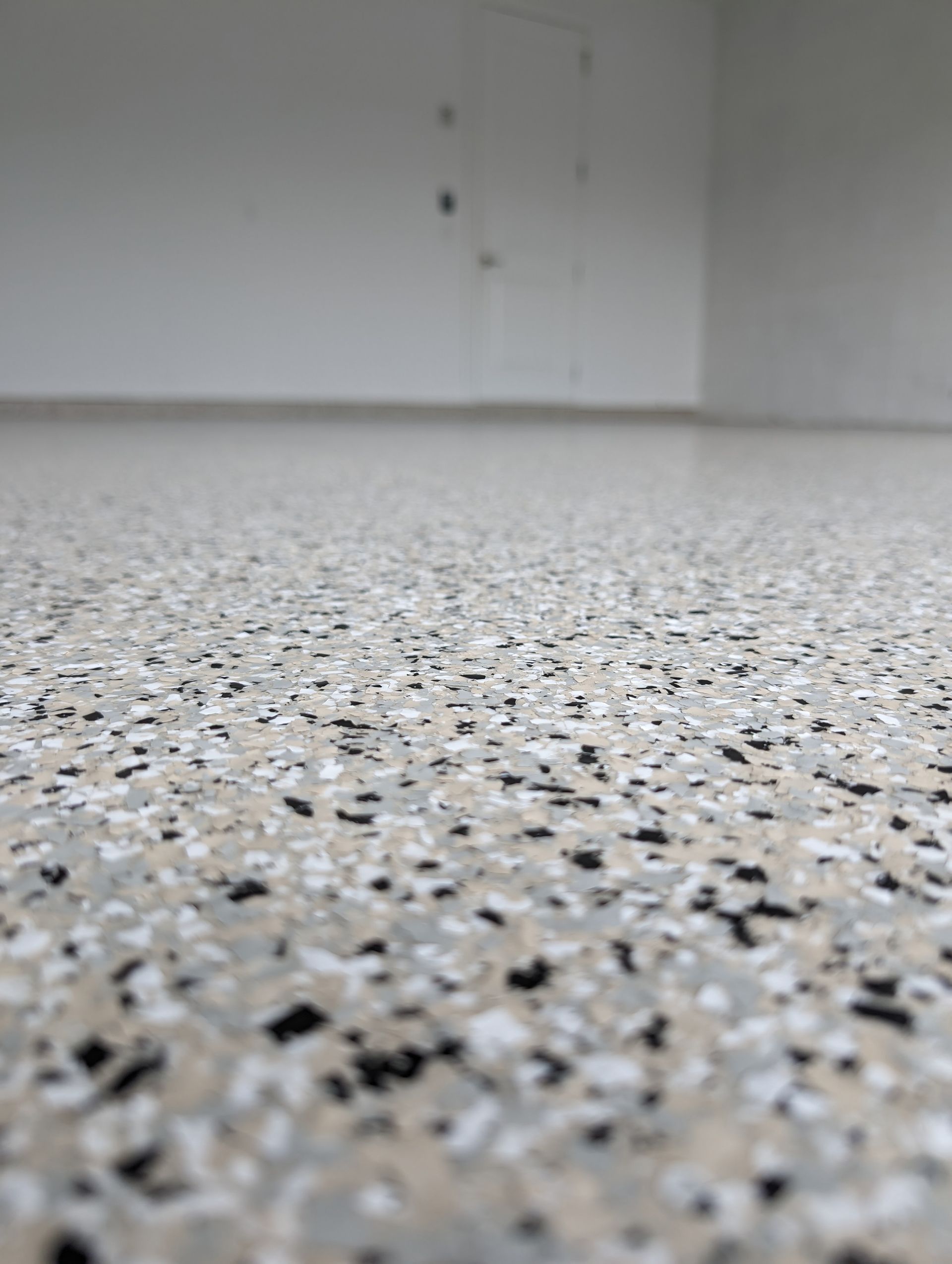 Empty speckled floor in a bright, unfurnished room with plain white walls.