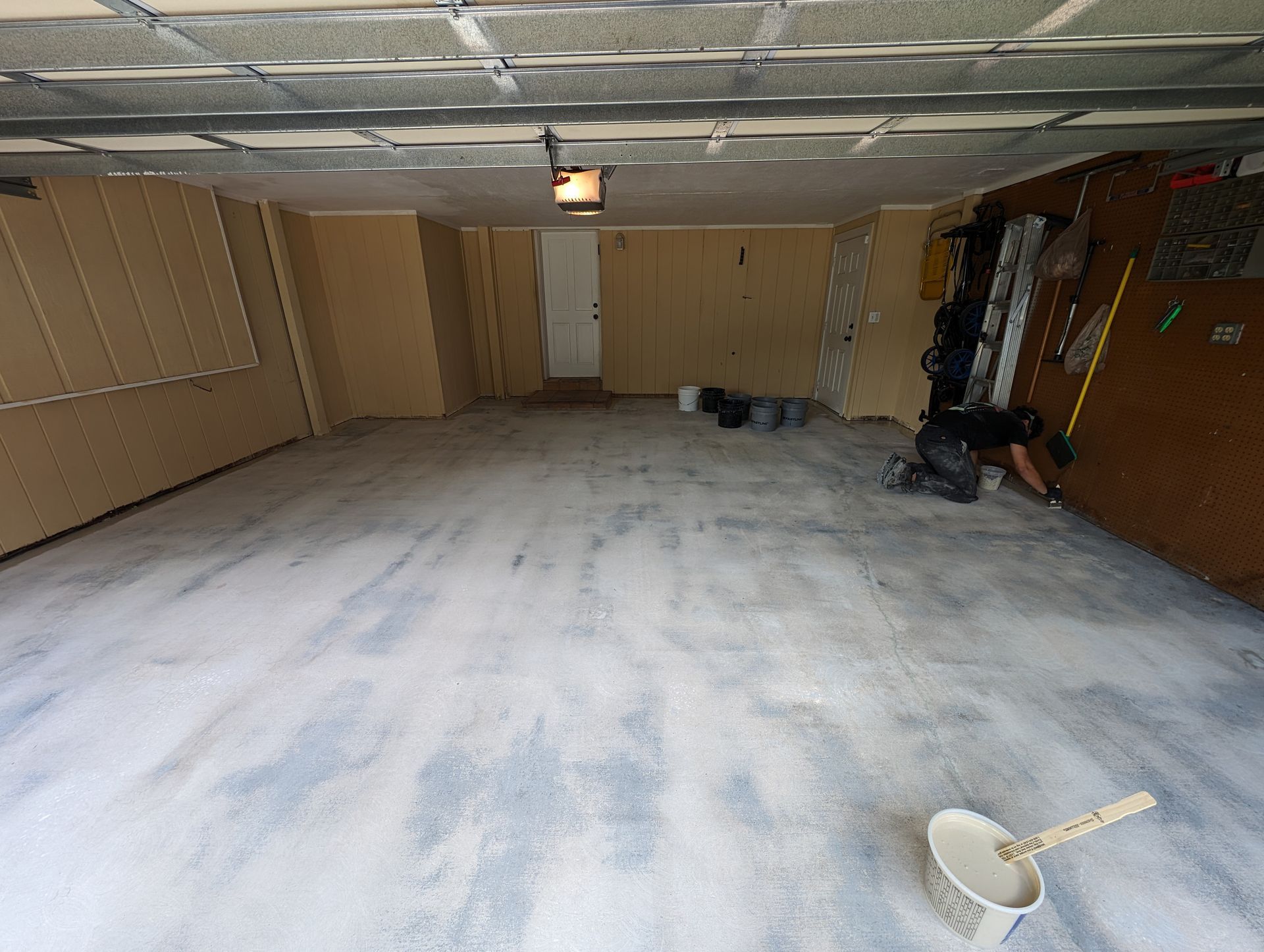 Empty unfinished room with beige walls, white tiled floor, ceiling light, and cleaning supplies near the right wall
