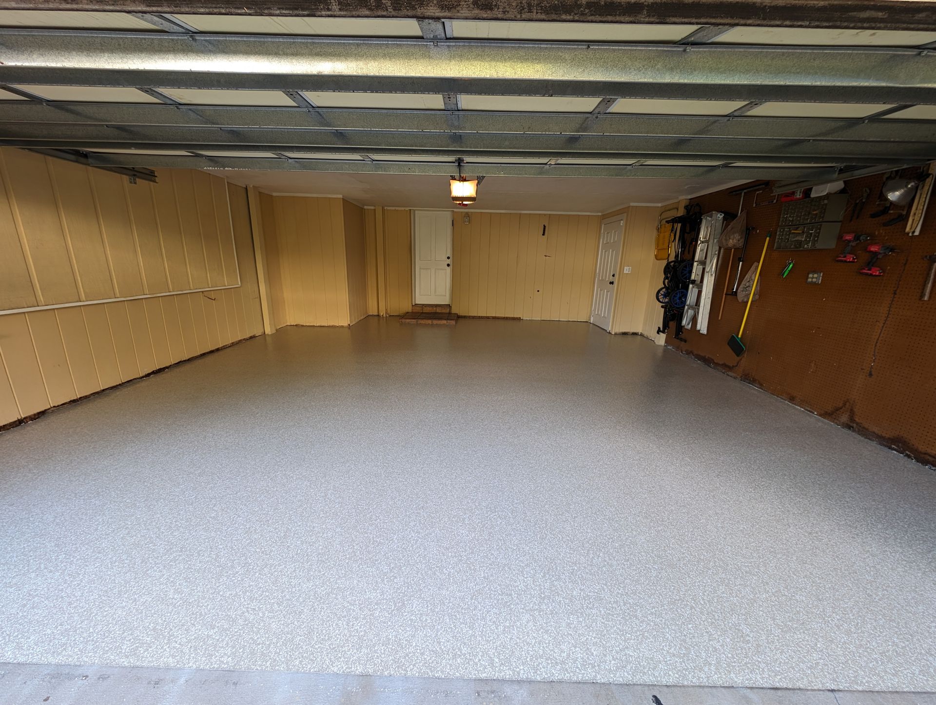 Empty garage with gray speckled floor, beige walls, and overhead door tracks visible.
