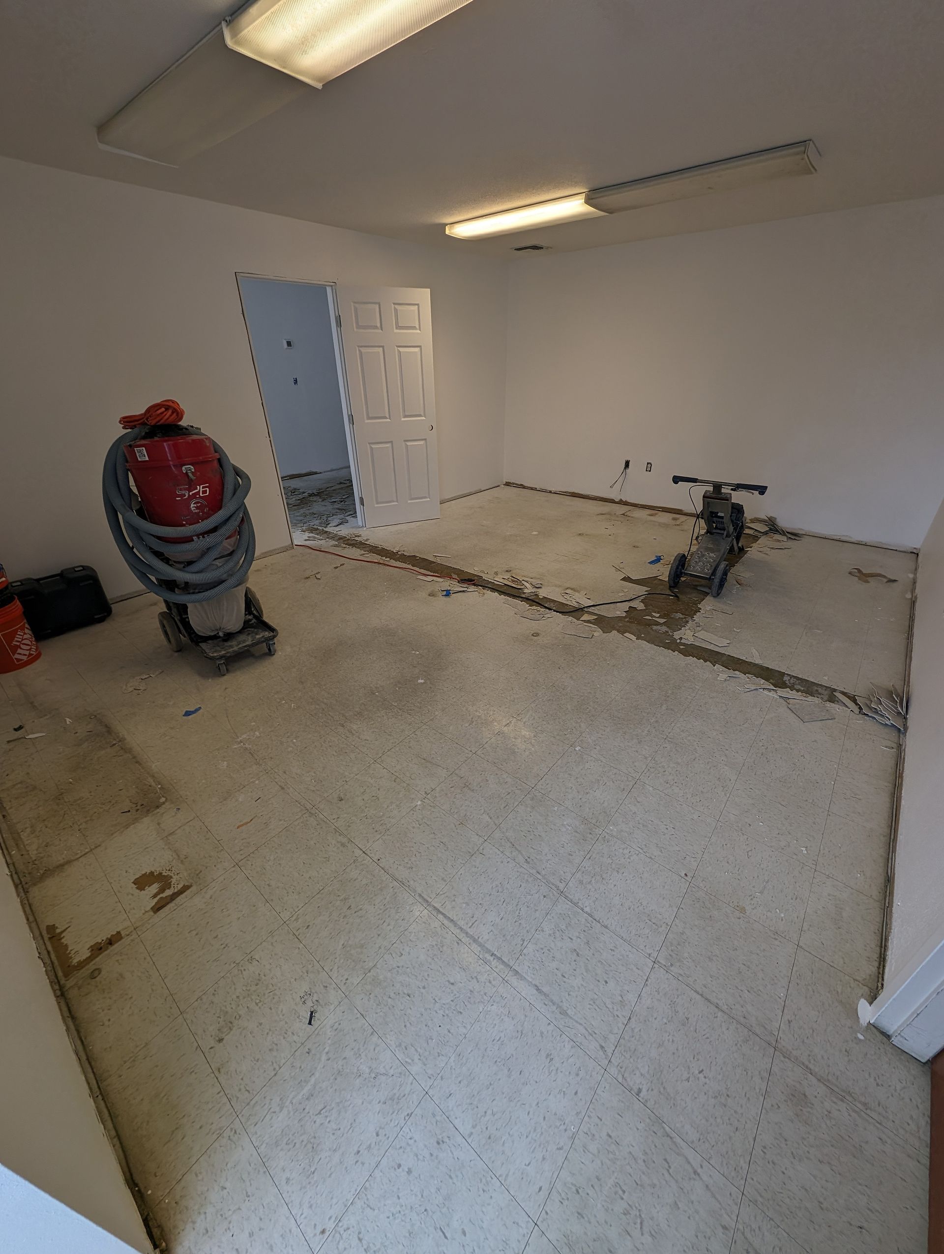 Empty garage with concrete floor, white walls, and construction equipment under fluorescent lights