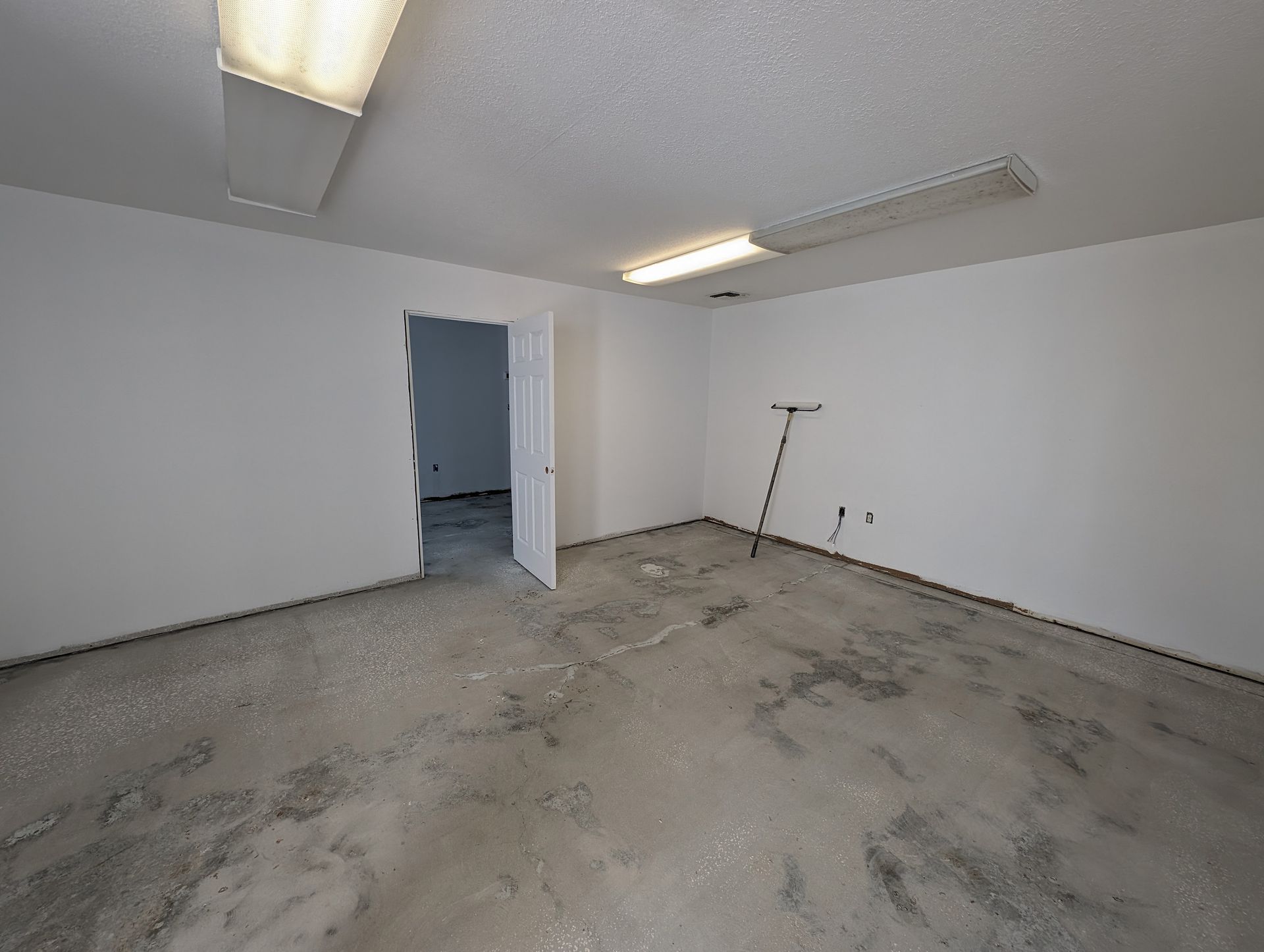 Empty unfinished garage with concrete floor, white walls, open doorway, and a leaning tool in the corner