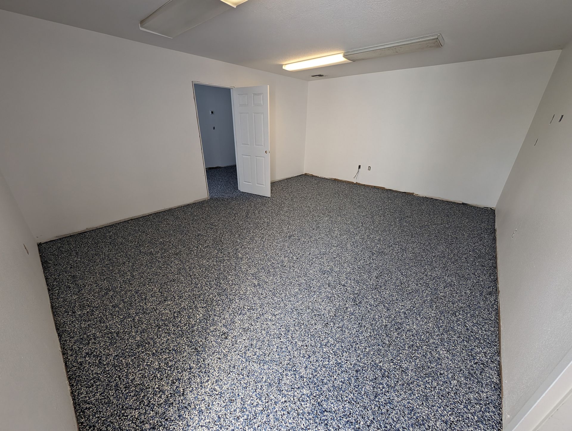 Empty carpeted room with white walls, a ceiling light, and an open doorway.