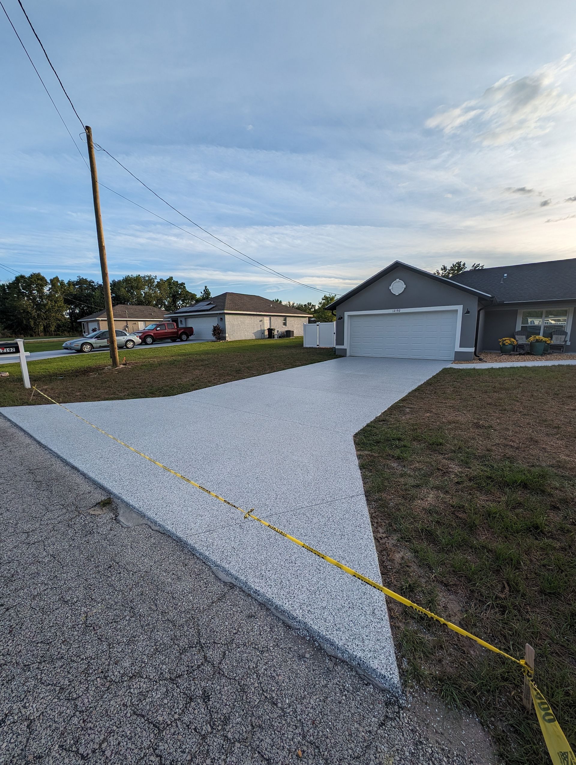 Concrete driveway leading to a gray garage beside a gravel road at dusk