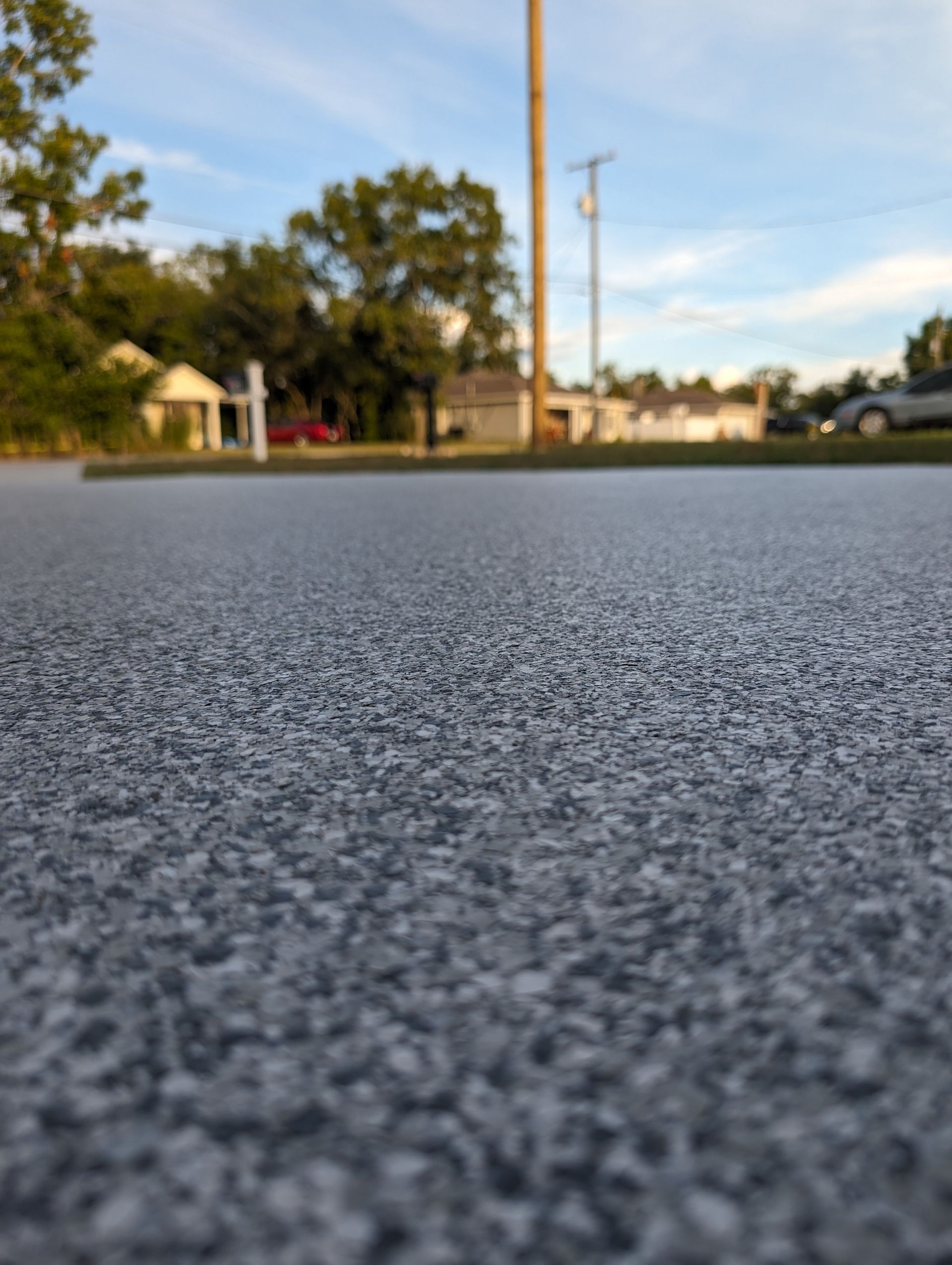 Close-up of textured asphalt road with houses and trees in the blurred background at sunset