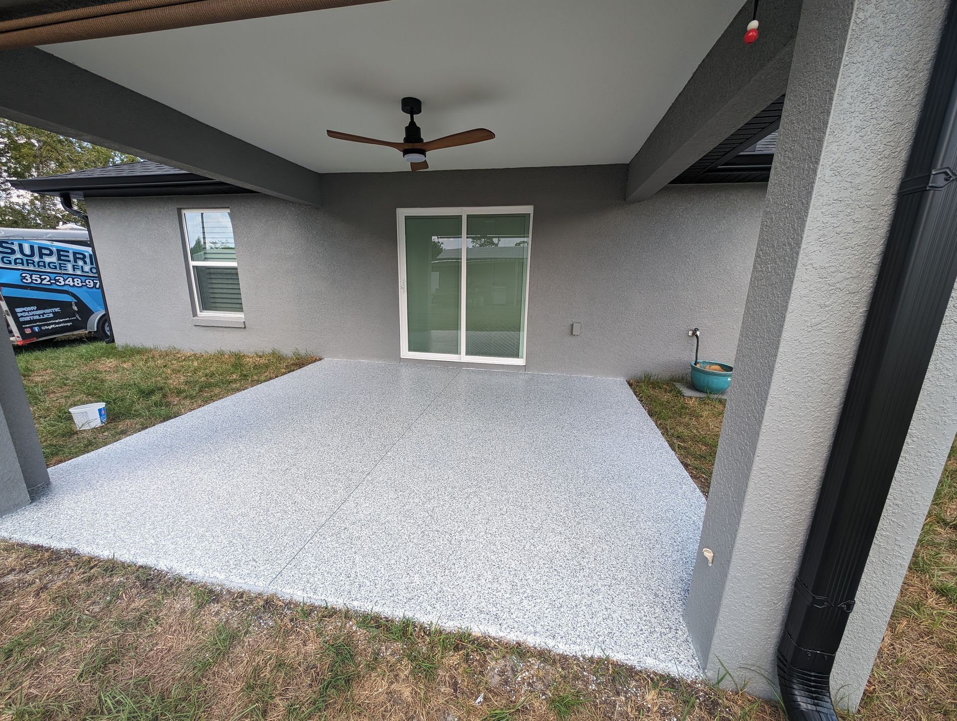 Covered concrete patio with ceiling fan, sliding glass door, and a small planter on the right.