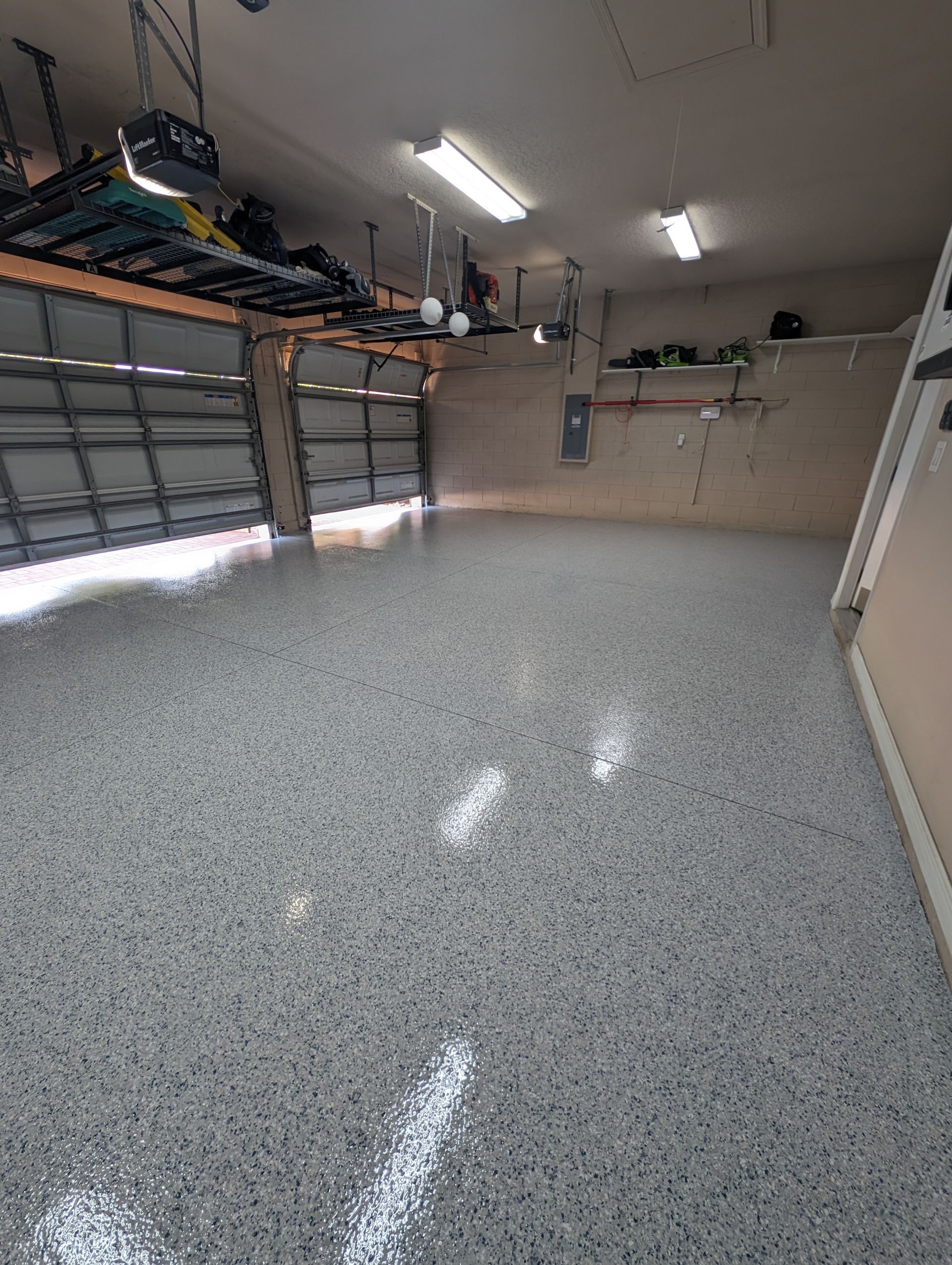 Empty garage with gray speckled epoxy floor and overhead storage shelves.