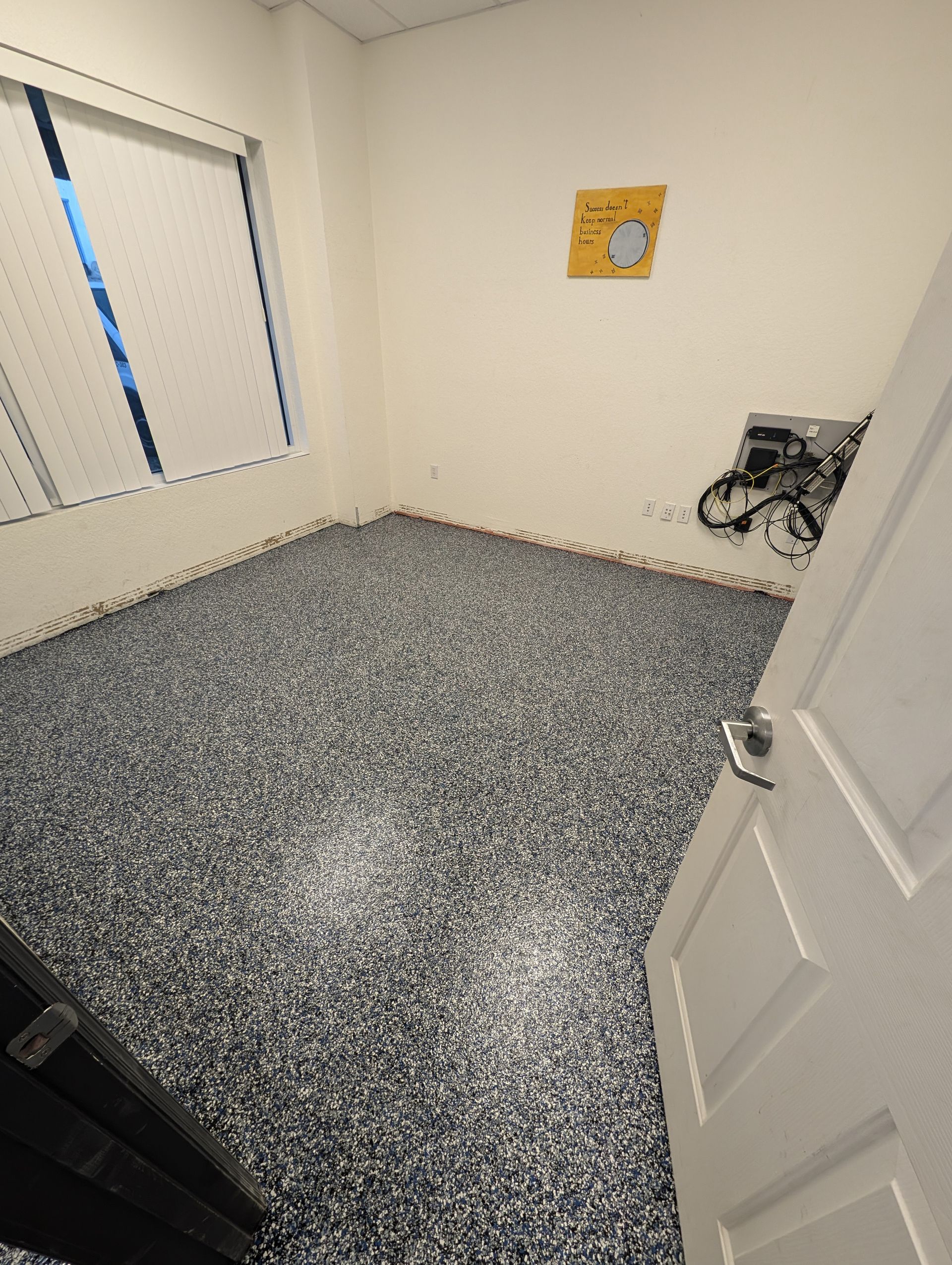 Empty room with speckled carpet, white walls, window blinds, and an open door.