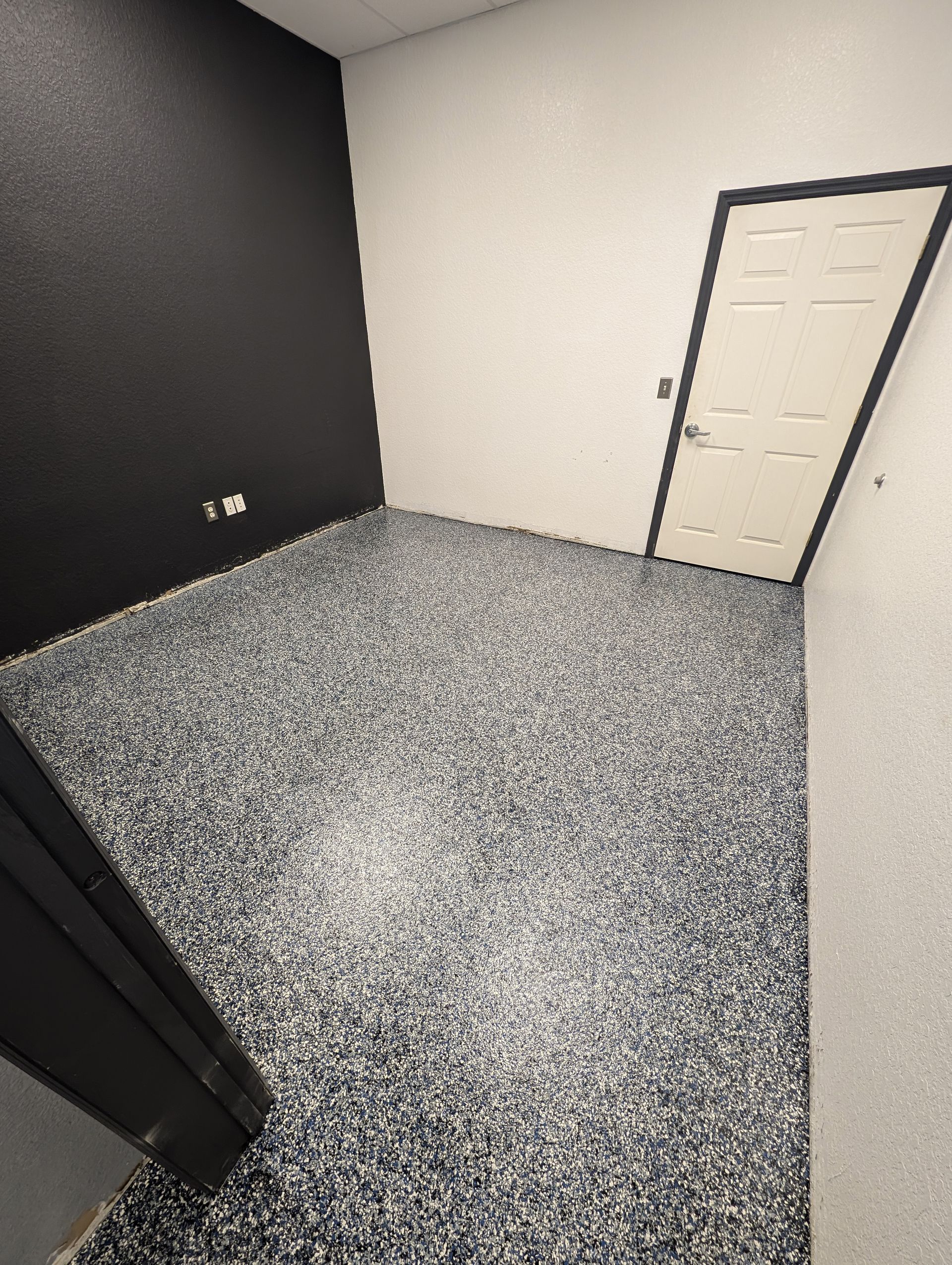 Empty gray-carpeted room with dark and light walls and a closed white door.
