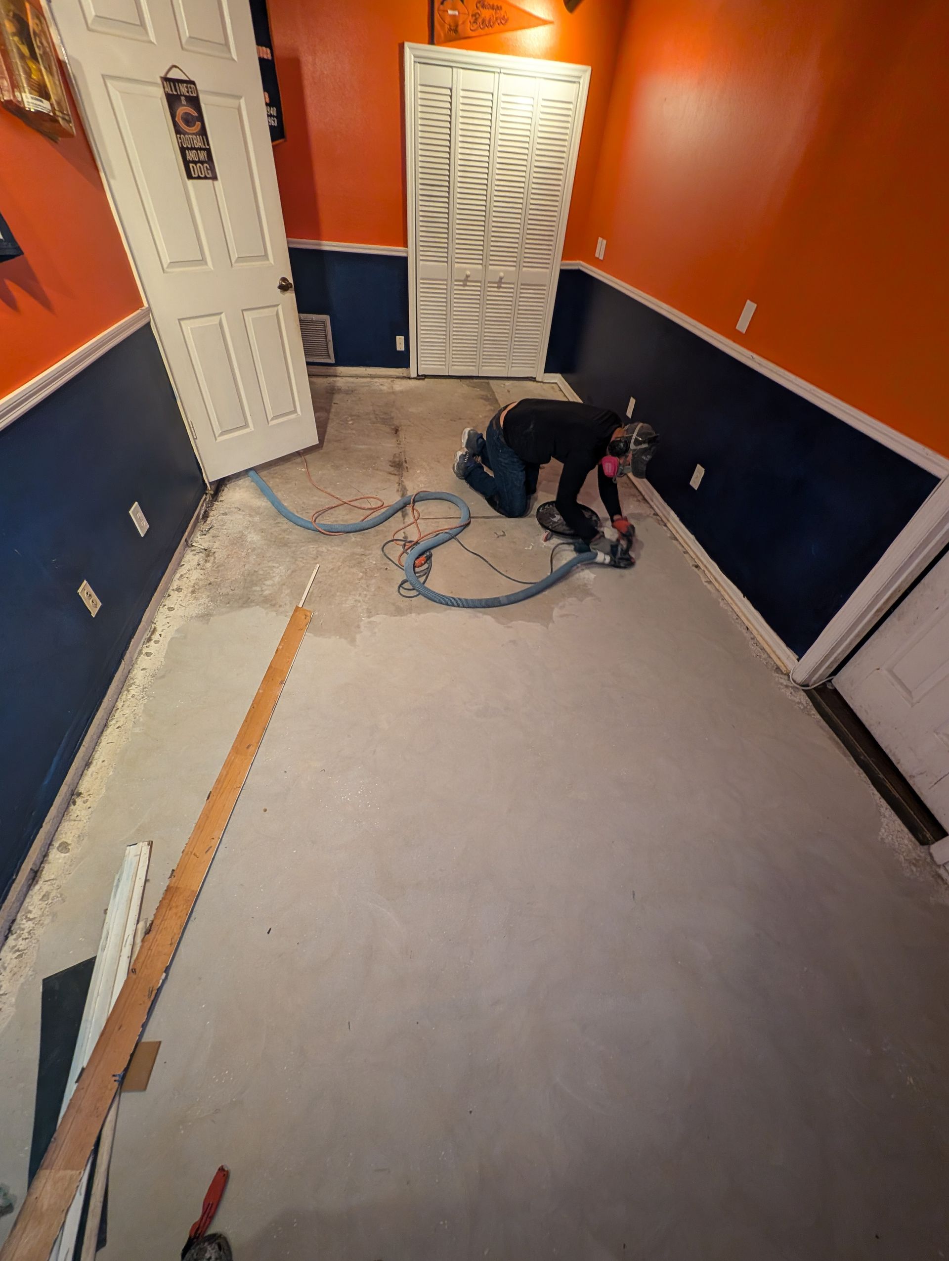 Person kneeling on a floor, working with a power tool in a small orange-and-blue room.