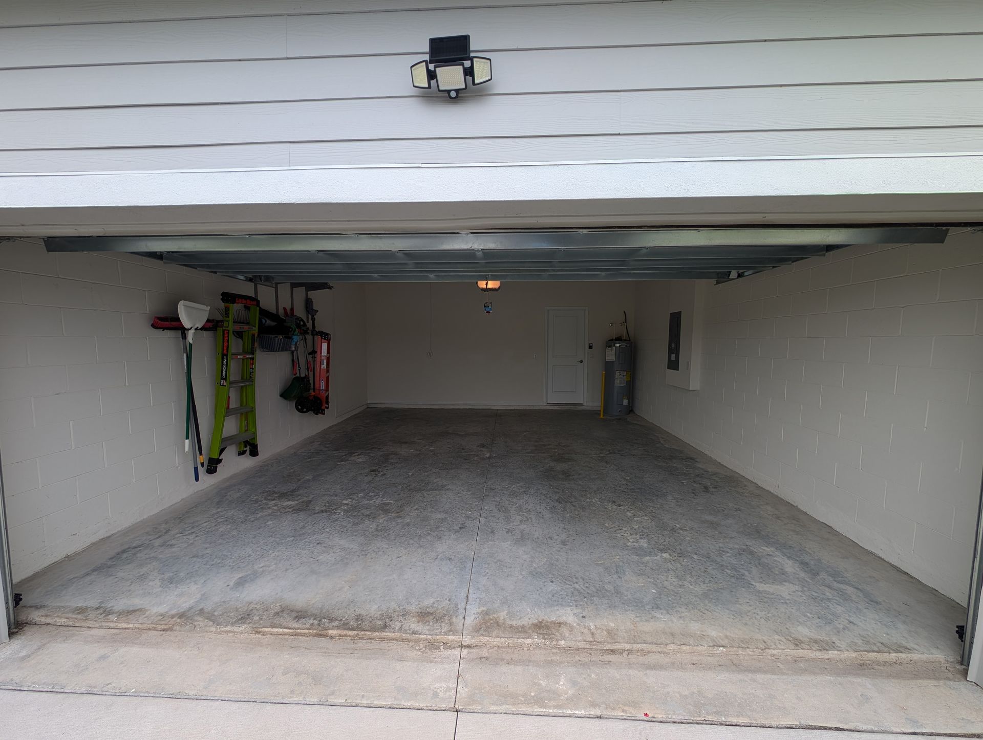 Open garage with a sloped concrete floor and wall-mounted tools on the left.