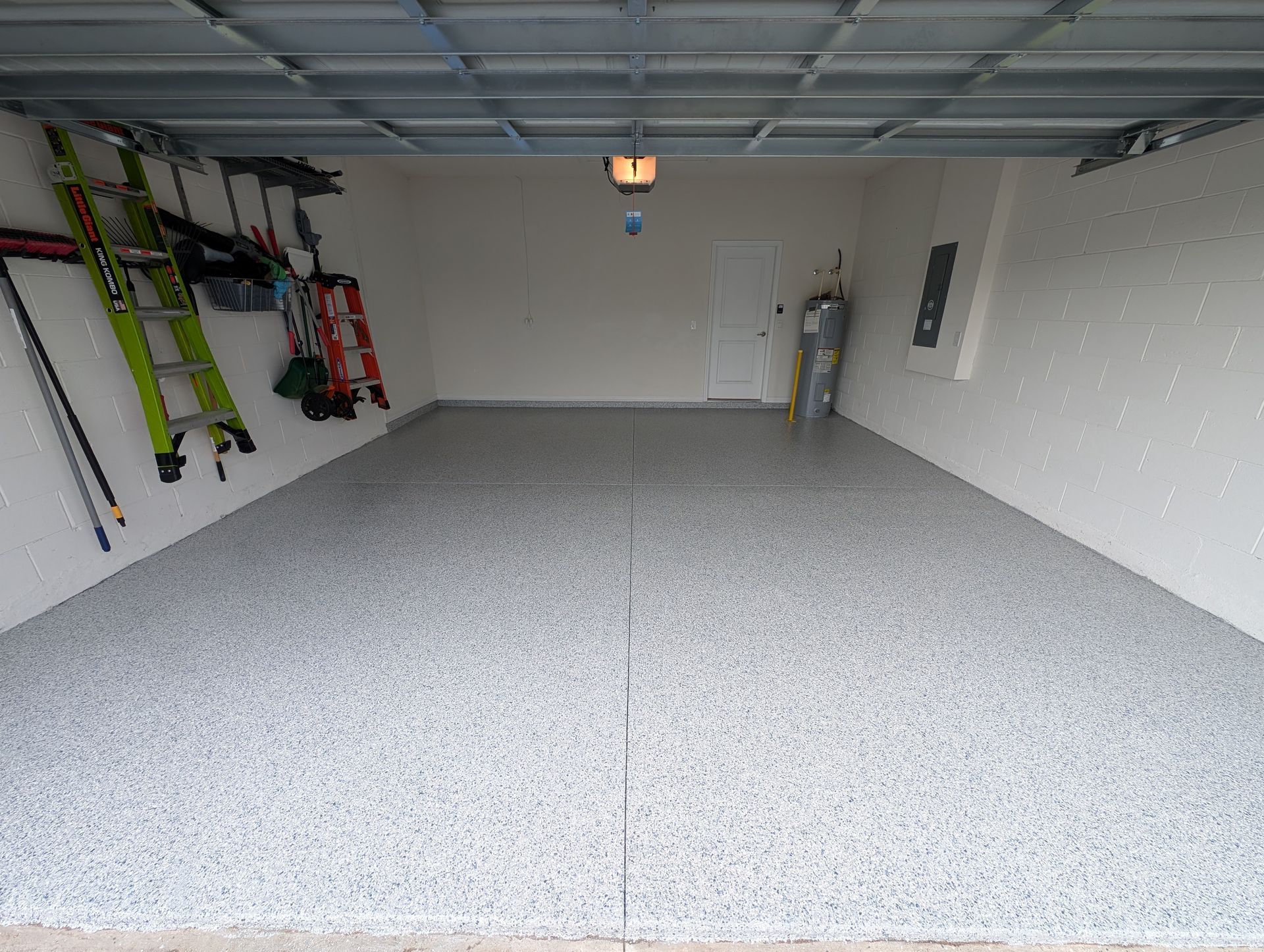 Empty garage with speckled floor, storage gear on the left wall, and a closed white door at the back.