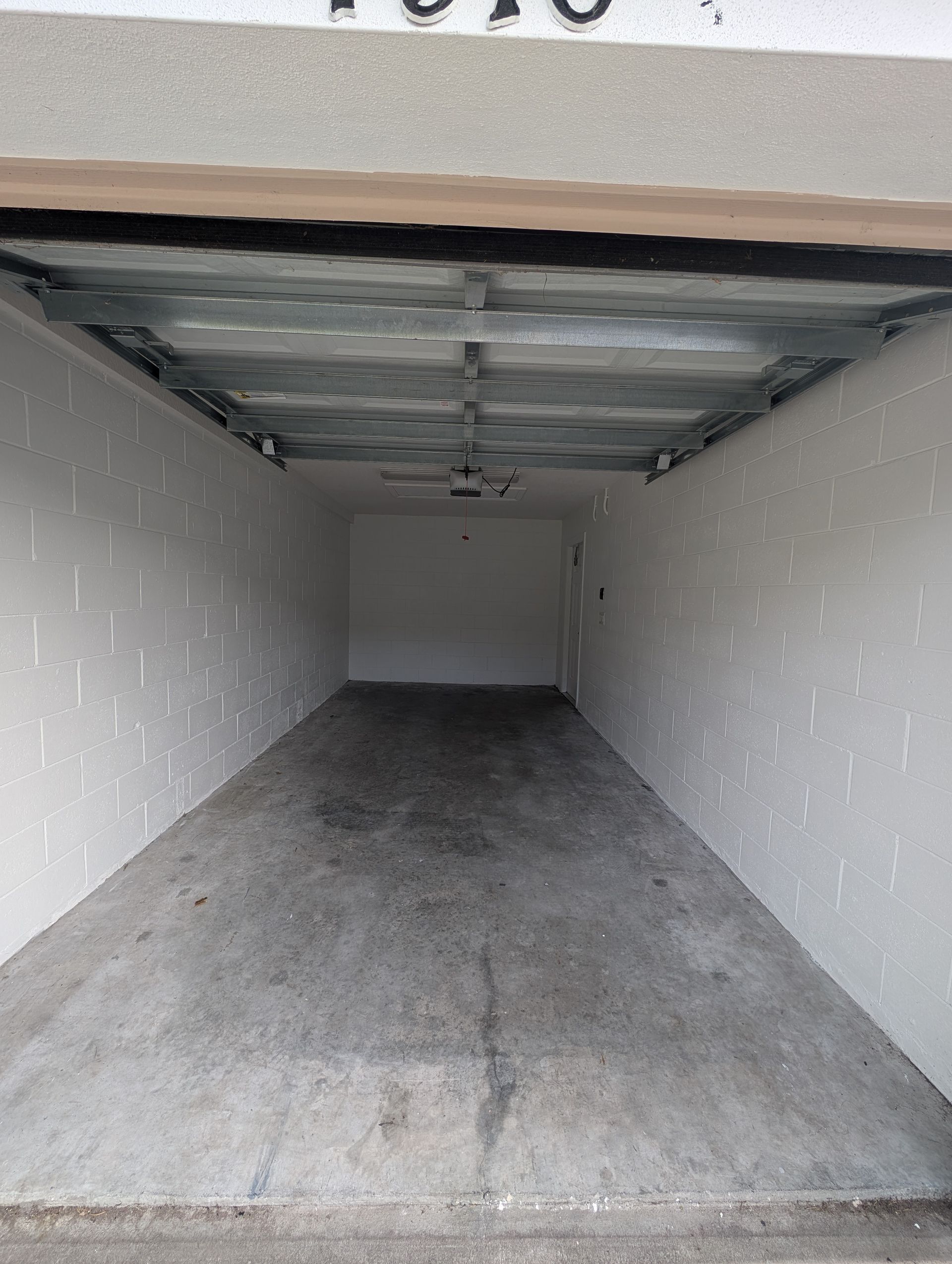 Empty garage interior with a concrete floor, white walls, and exposed ceiling panels