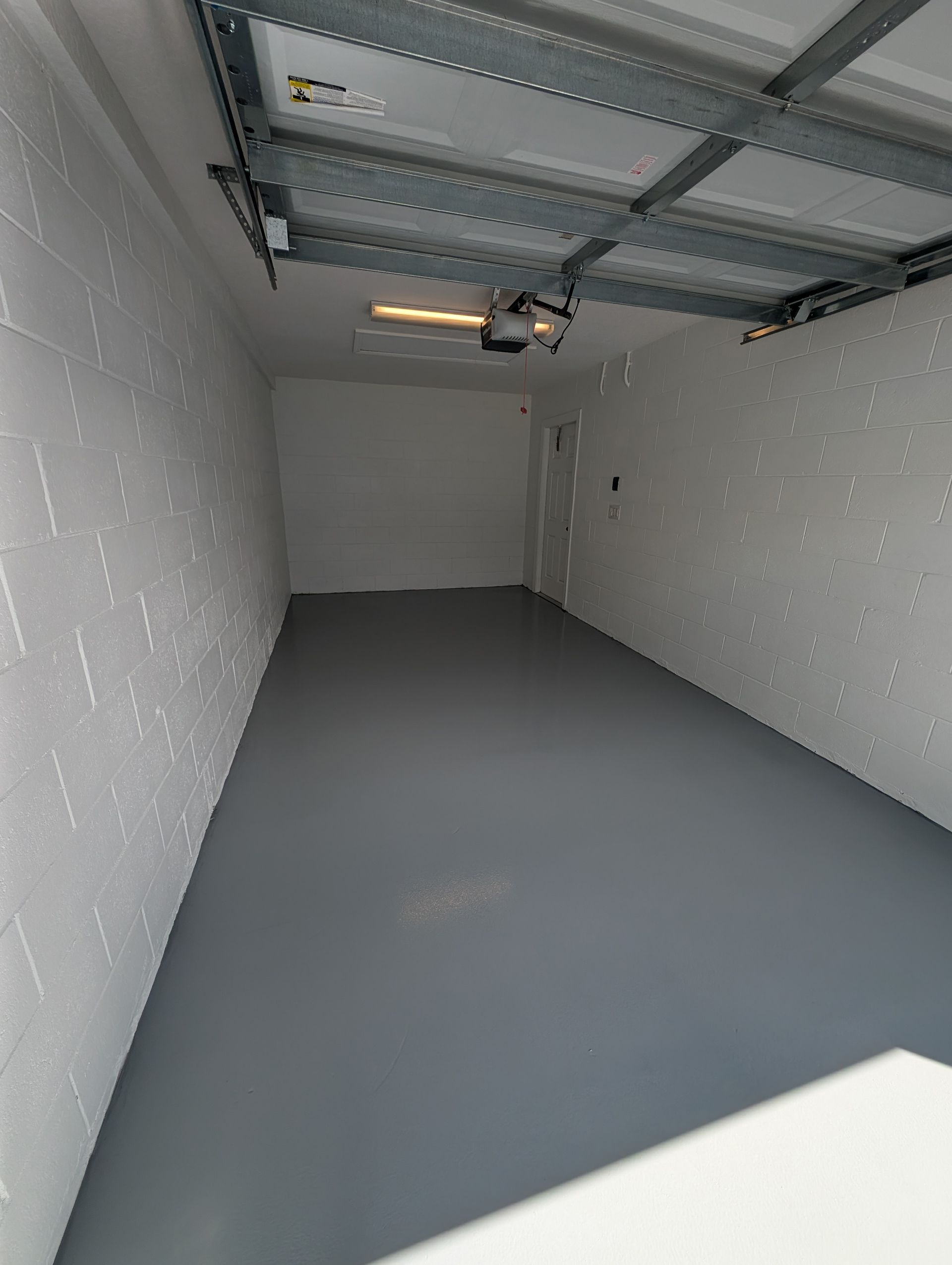 Empty garage interior with gray floor, white walls, and an open ceiling door track.