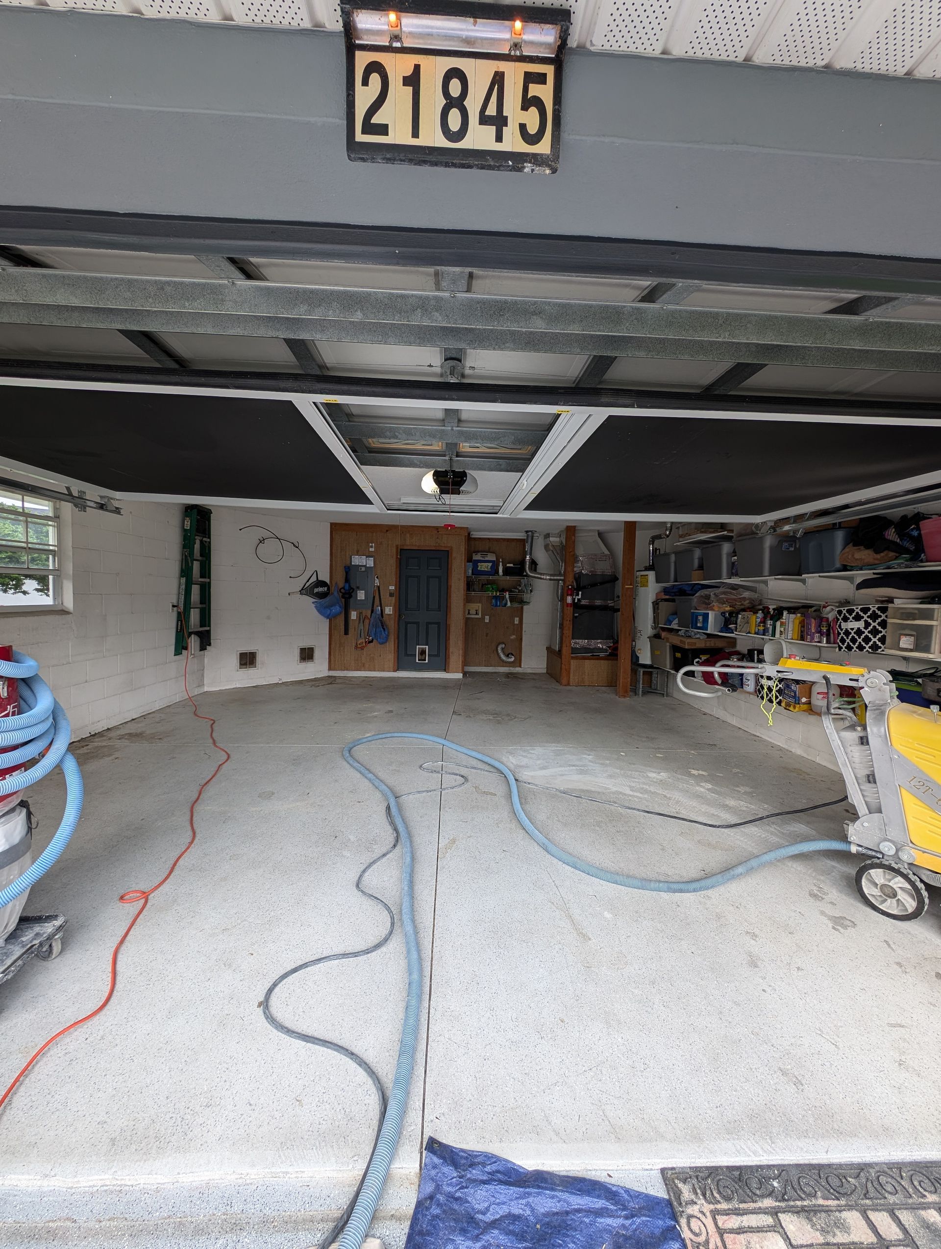 Open garage with gravel floor, hanging cords, shelves, and a license plate above the door.