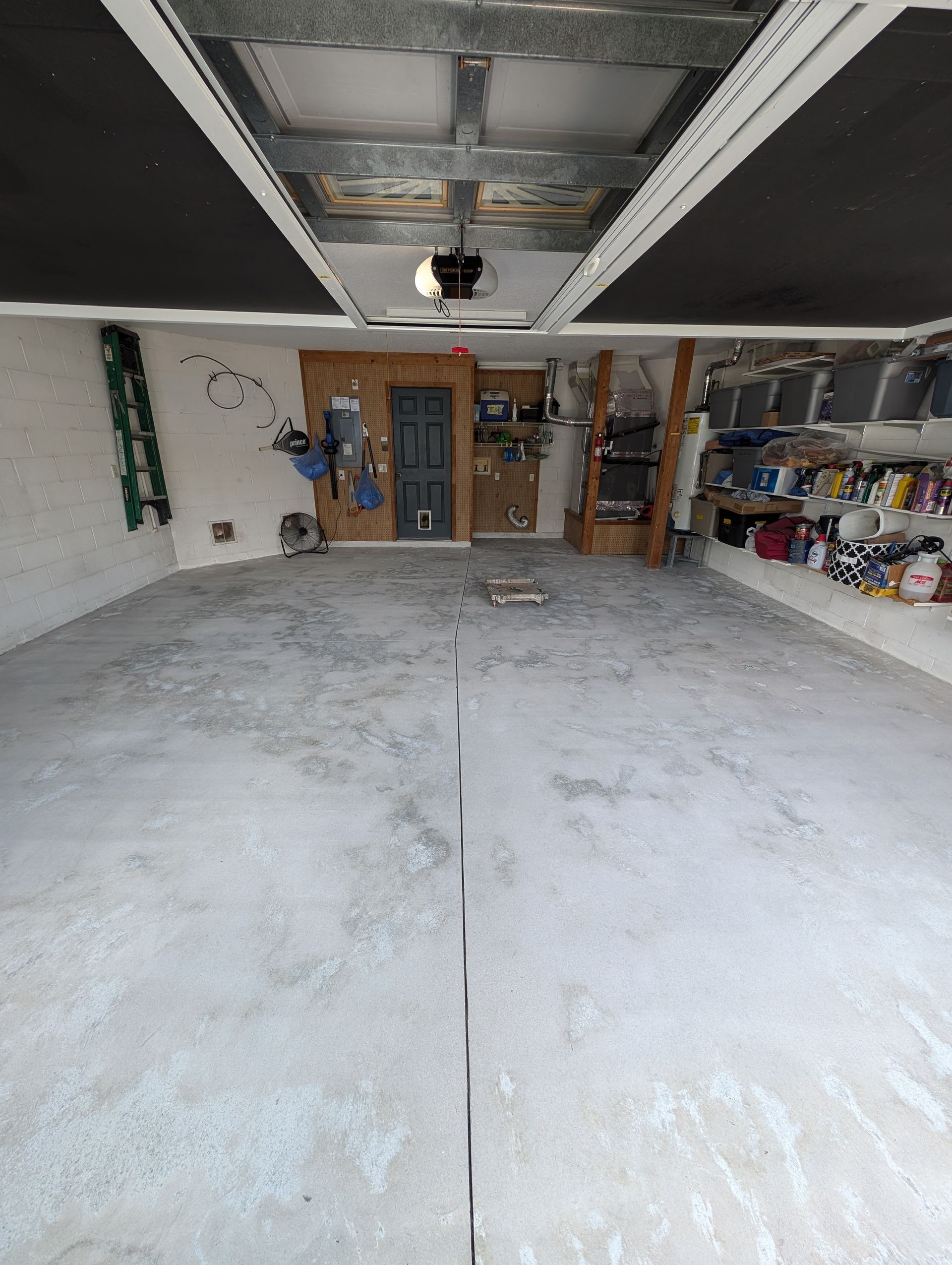 Empty garage with a concrete floor, overhead door tracks, and storage shelves along the back and right walls.