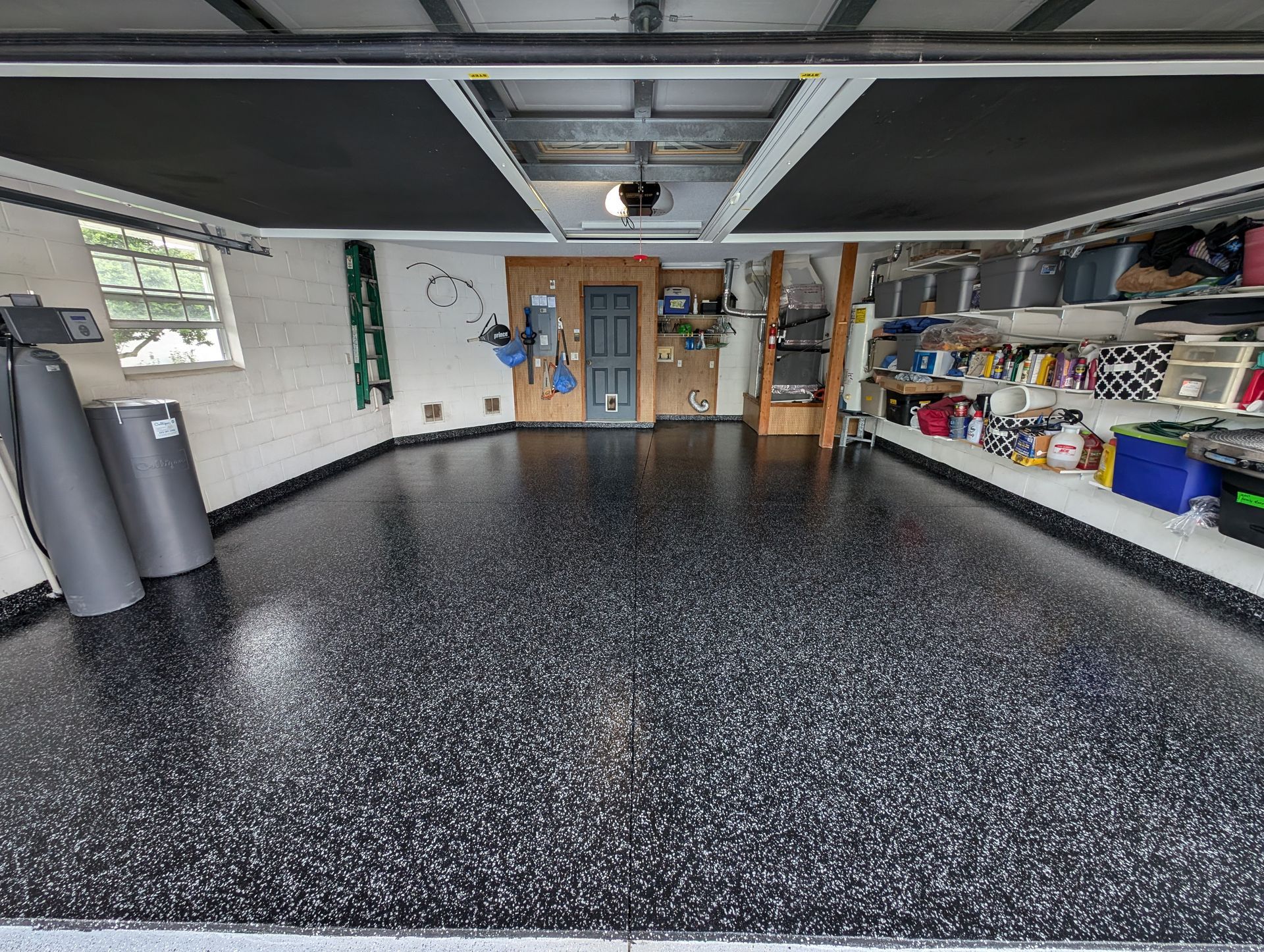 Spacious garage with black speckled floor, open storage shelves, and wooden double doors.