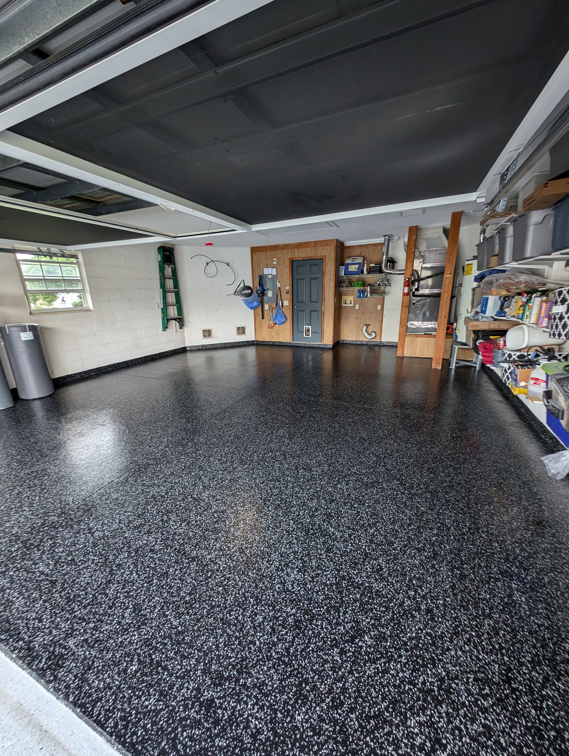 Empty garage with black speckled floor, shelves, and a wooden door under a dark ceiling.